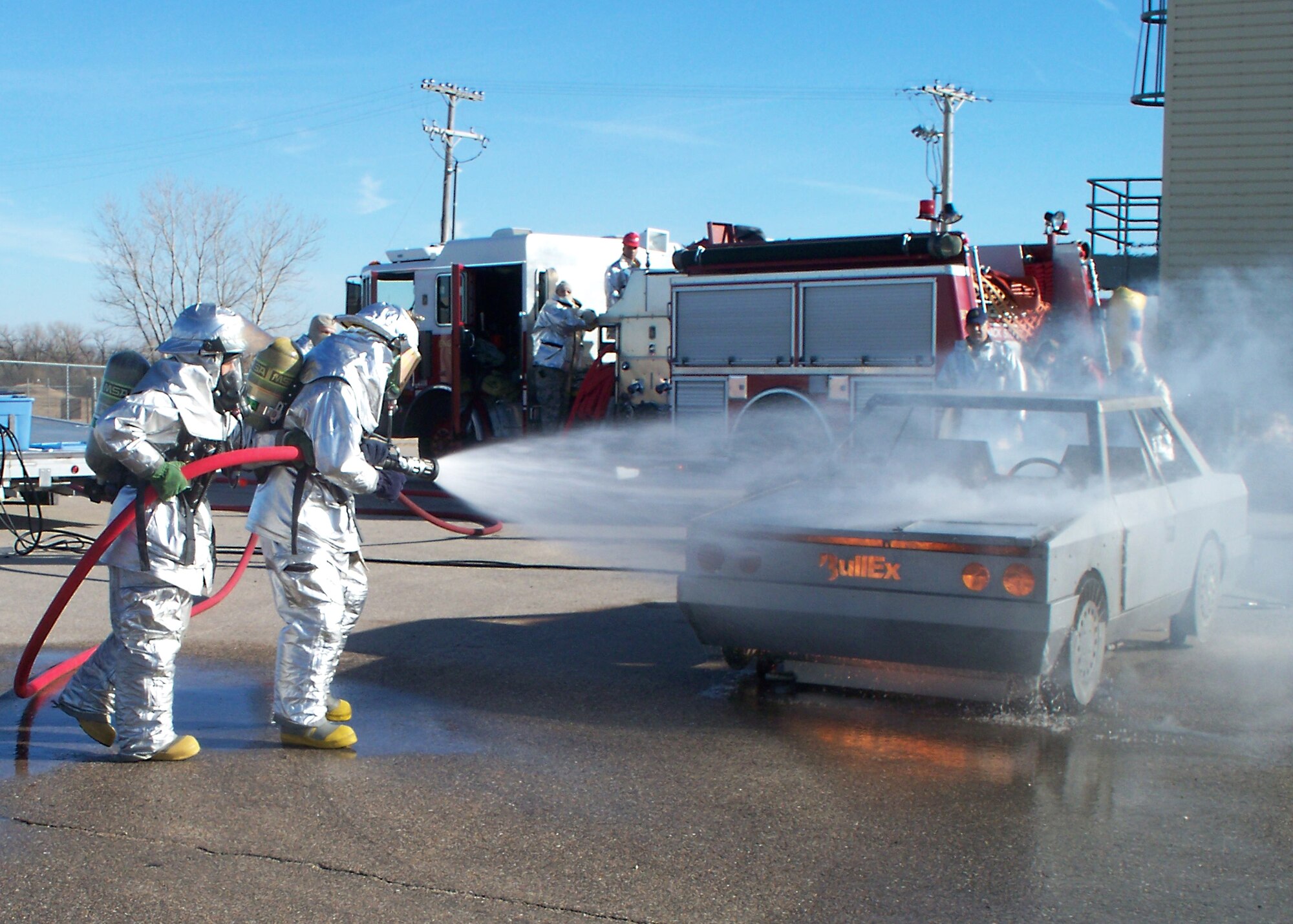 McConnell firefighters approach a portable car fire trainer to douse a simulated engine fire at the fire training area, Dec. 16, 2010, McConnell Air Force Base, Kan. The car trainer replicates various vehicle fire emergencies such as engine, multiple passenger compartment and fuel spill fires. The simulator allows the operator to safely control the training scenario fires. (courtesy photo)