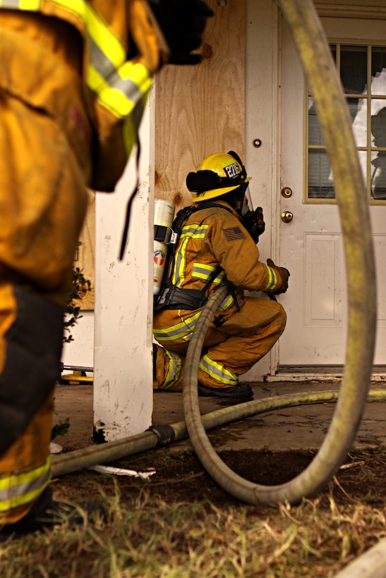 Firefighters from Camp Pendleton Fire Department and North County Area Fire Departments prepare to demonstrate a firefighting technique called positive pressure attack during simulated fire scenarios in the old base housing units at Naval Weapons Station Fallbrook, Jan. 6. Since the old structures were scheduled for demolition, the U.S. Navy donated them to the fire departments to use for advanced training.