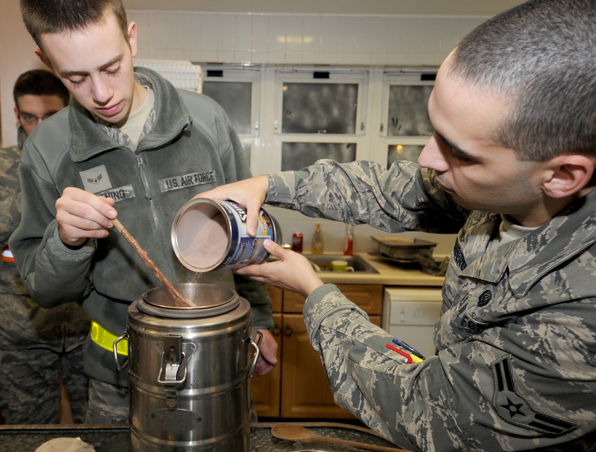 RAF MILDENHALL, England -- Airman 1st Class Kent Casting, 100th Communication Squadron client systems technician, stirs as Airman 1st Class Chris Winemberg, 100th CS information assurance officer, adds mix to hot chocolate here Jan. 7, 2011. Airmen from across RAF Mildenhall volunteered to prepare and distribute hot chocolate to the 100th Security Forces Squadron "Defenders" working at gates in the rain.  (U.S. Air Force photo/Senior Airman Tabitha M. Lee)