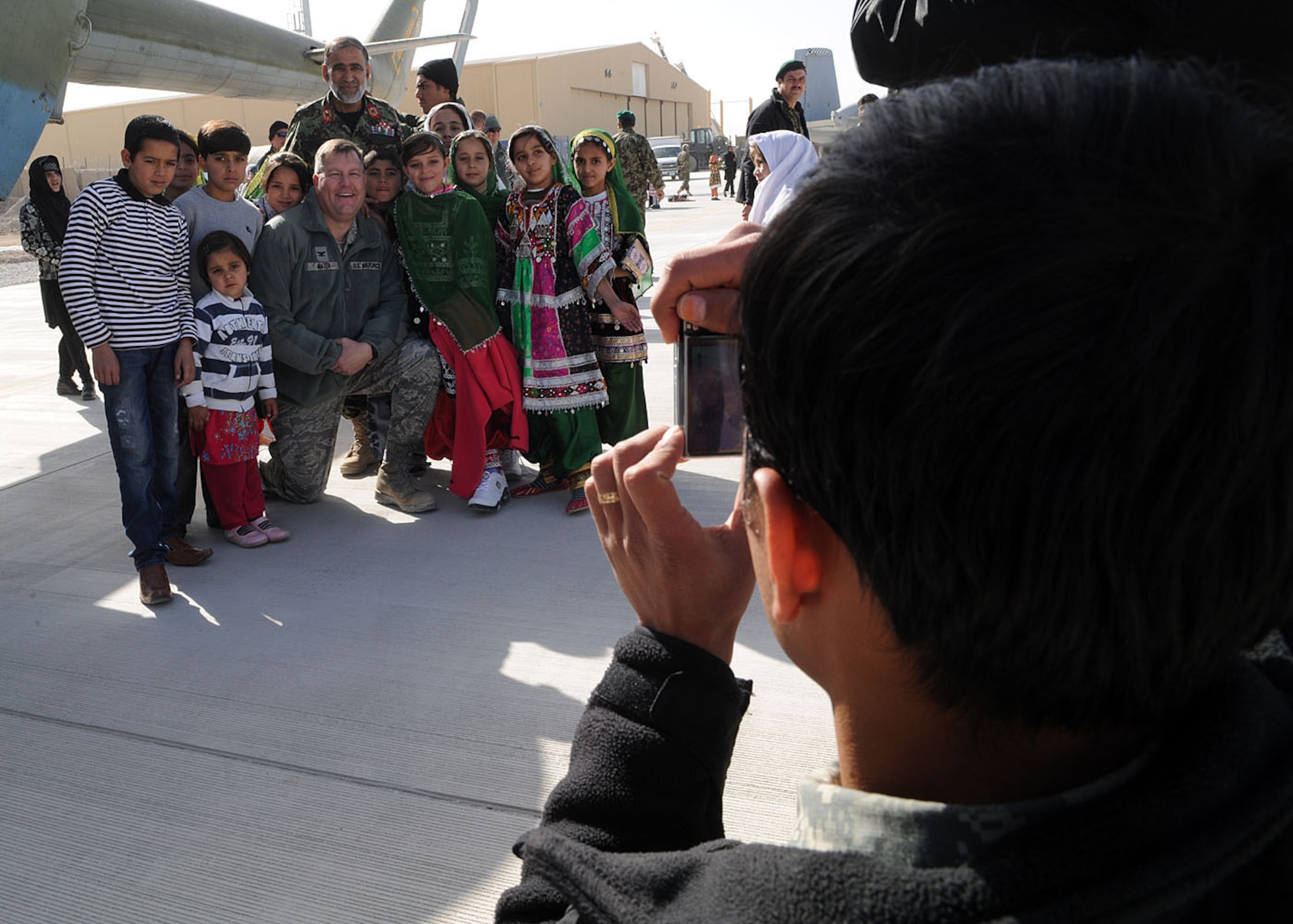 An Afghan citizen takes a photograph of school children posing with Col. Bernard Mater, 738th Air Expeditionary Advisory Group commander, and Afghan Air Force Brig. Gen. Mohammed Yousuf, Kandahar Air Wing vice commander, during the KAW open house at Kandahar Airfield, Afghanistan, Jan. 1. The open house showcased the newly-constructed facilities and the inventory of the force. Coalition forces, tribal elders and school children attended the event to foster the continued partnership between the Afghan National Security Forces and International Assistance Security Force. (U.S. Air Force photo by Senior Airman Daryl Knee / 16th Mobile Public Affairs Detachment)