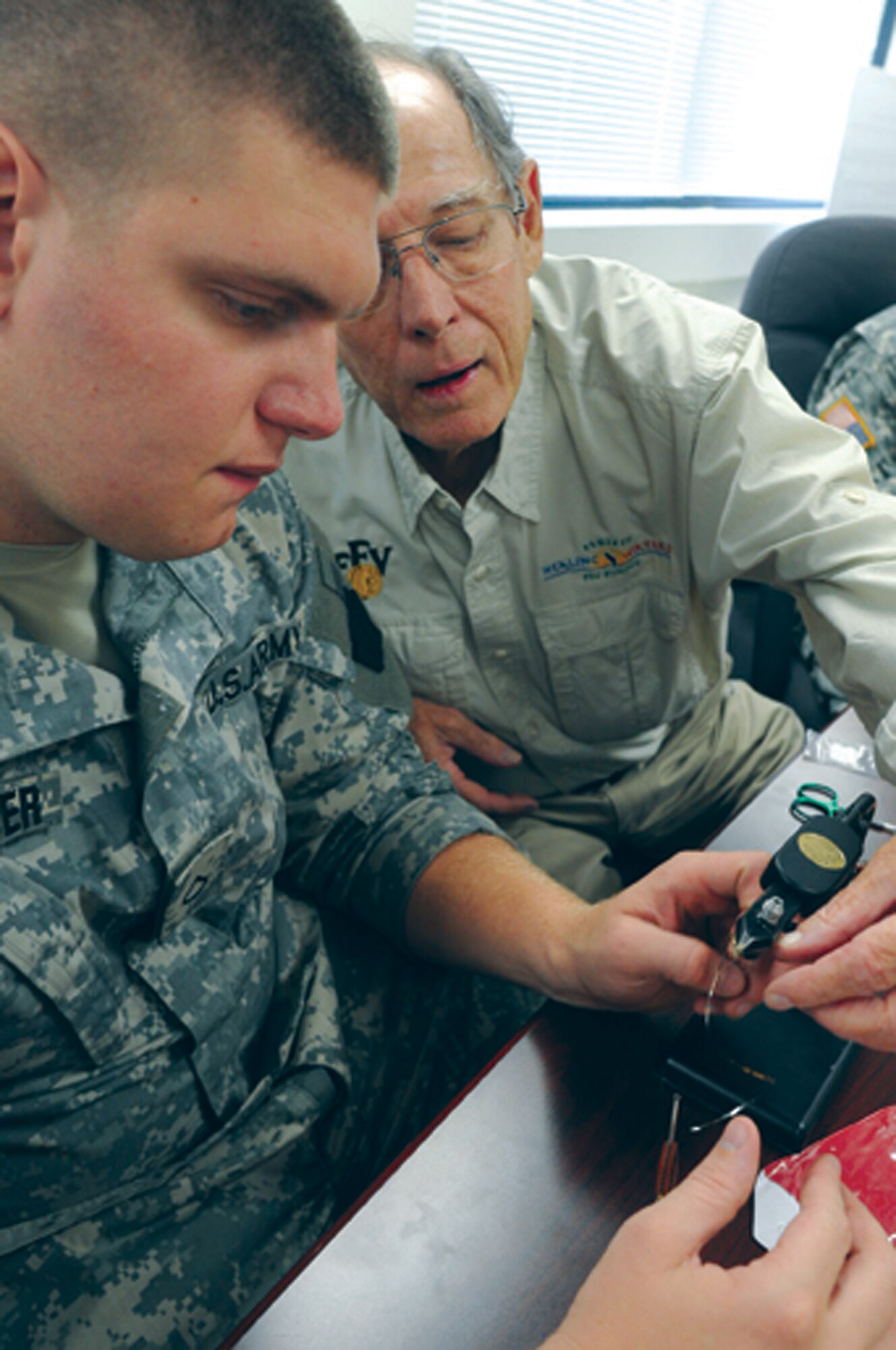 Spc. Josh Humberger looks on as Project Healing Waters volunteer and Fly Fishers of Virginia member Alan Hooker demonstrates a fly-tying technique during a fly-tying clinic at the Fort Eustis Warrior Transition Unit.