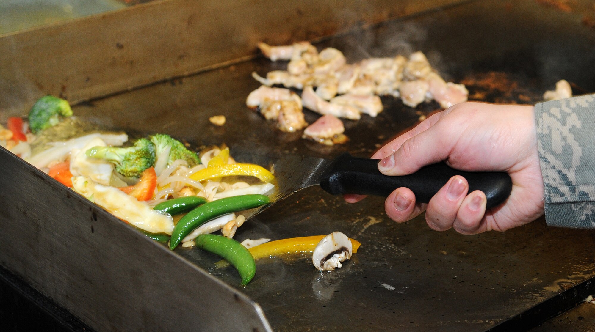 RAF MILDENHALL, England -- Airman 1st Class Jessica Ashe, 100th Force Support Squadron services apprentice, cooks stir-fry Jan. 11, 2011 during a Mongolian Barbeque at the Gateway Dining Facility.  Next month, the dining facility will be visited by a committee to assess them for the Air Force Hennessy Evaluation. (U.S. Air Force photo/Senior Airman Tabitha M. Lee)