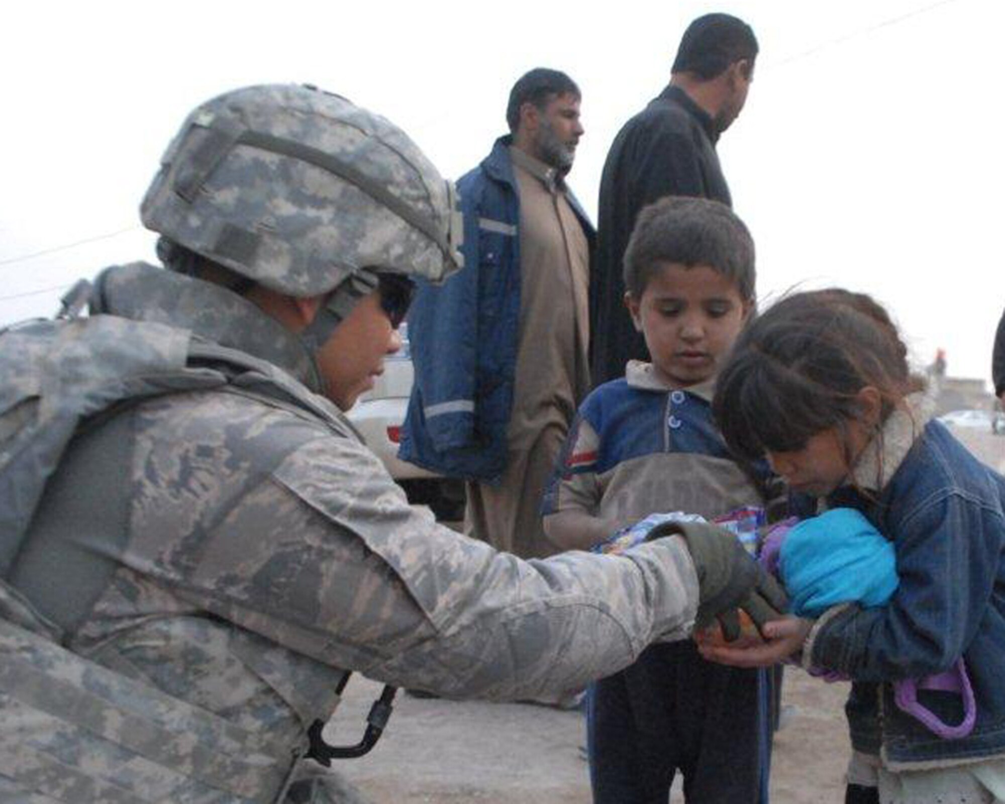 U.S. Air Force Master Sgt. Luis Buot, Echelon Above Division-Advise and Train maintenance advisor and Pemberton, N.J., native, gives candy to two local Iraqi children Dec. 16 at Ur Elementary School near Tallil Air Base, Iraq. Sergeant Buot is deployed from Joint Base McGuire-Dix-Lakehurst, N.J. (U.S. Army photo by Spc. Chastity Boykin)