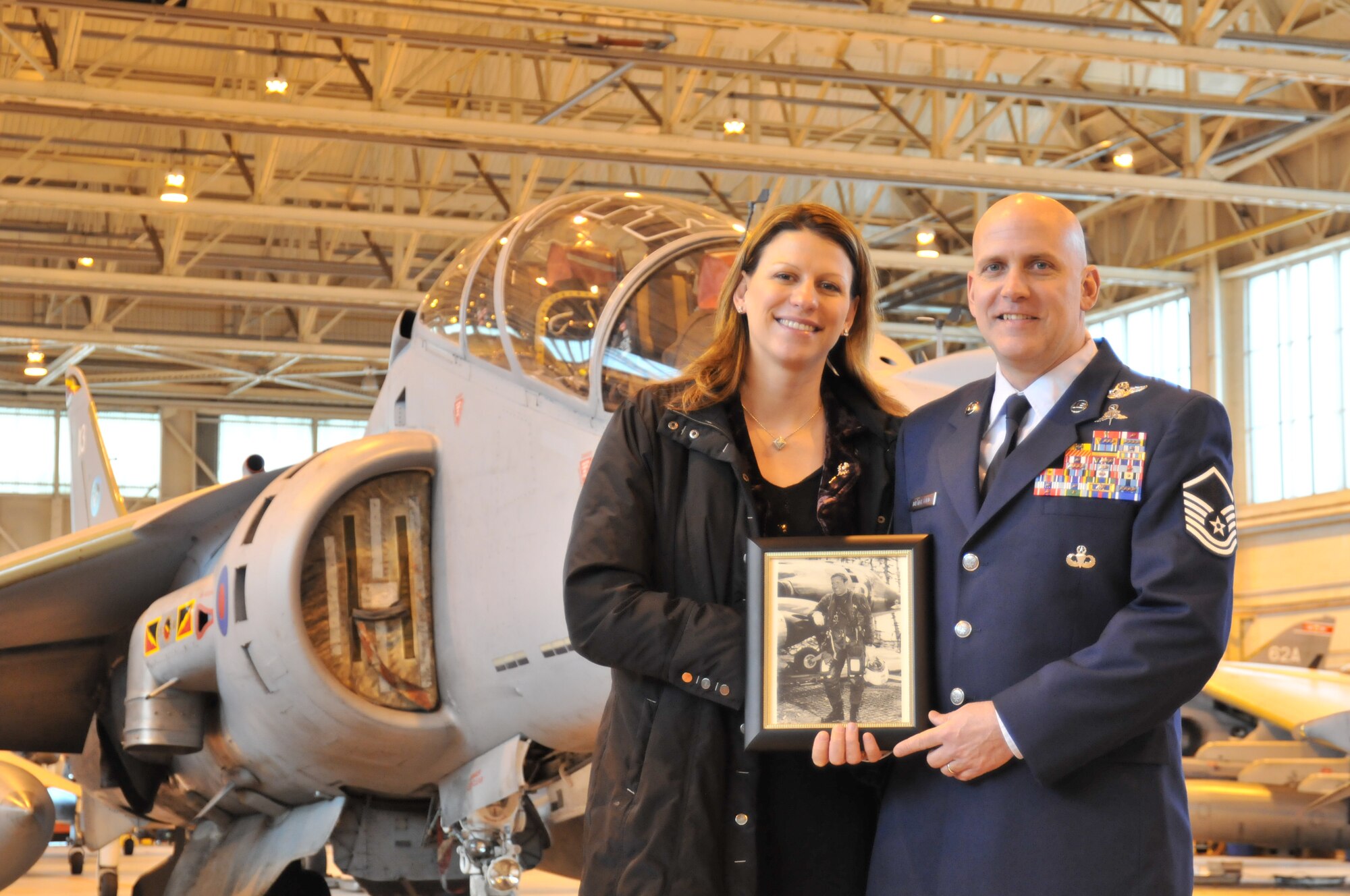 ROYAL AIR FORCE COTTESMORE, England – Master Sgt. Louis Distelzweig, a pararescueman with the 56th Rescue Squadron at RAF Lakenheath, and his wife, Eve, pose with a picture of Sergeant Distelzweig’s father, Capt. Louis Distelzweig Jr., in front of a Royal Air Force Harrier jet Jan. 11. Captain Distelzweig was a decorated pilot who perished in an aircraft accident in 1970 while serving as an exchange pilot with the RAF. (U.S. Air Force photo/Senior Airman David Dobrydney)