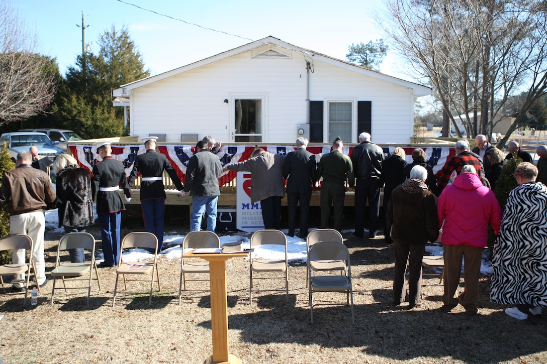 Beulaville, N.C. volunteers, Military Missions in Action members and Marines join hands around the Cottrell residence during the houses' dedication ceremony of the newly renovated house in Beulaville, N.C., Jan. 14. Warren Cottrell, a medically-retired sergeant with Post Traumatic Stress Disorder and Traumatic Brain Injury, and his family were the recipients of a free house renovation by MMIA, a non-profit organization dedicated to aiding in modifying wounded service members' homes, and volunteers from the community.