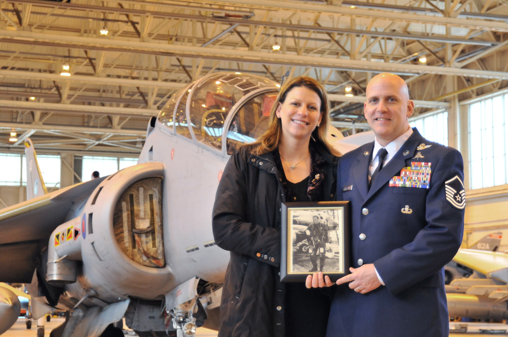 Master Sgt. Louis Distelsweig and his wife, Eve, pose with a picture of Sergeant Distelsweig's father, Capt. Louis Distelsweig Jr., in front of a Royal Air Force Harrier jet Jan. 11, 2011, at Royal Air Force Cottesmore, England. Captain Distelsweig was a decorated pilot who perished in an aircraft accident in 1970 while serving as an exchange pilot with the Royal Air Force. (U.S. Air Force photo/Senior Airman David Dobrydney)
