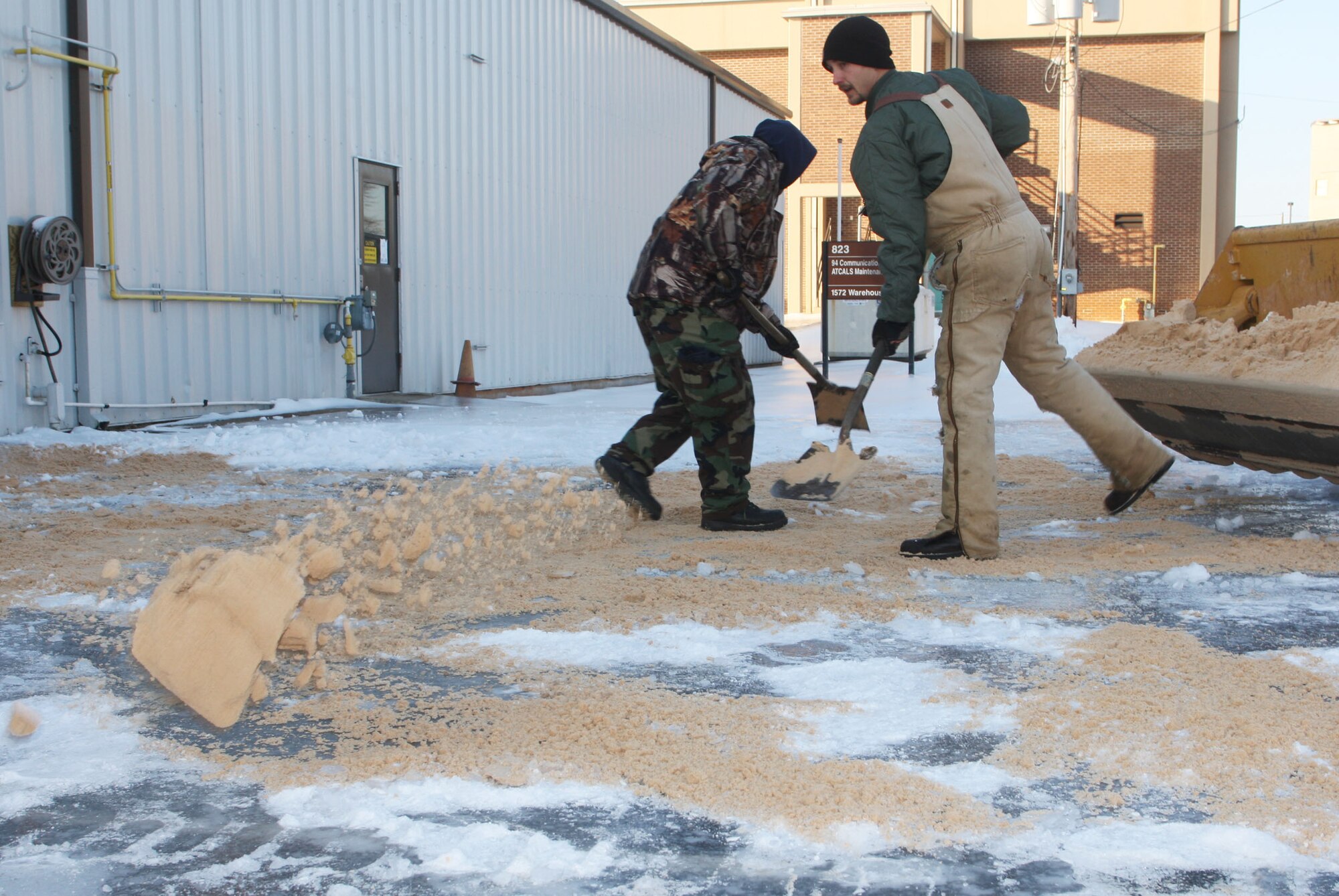 Grounds crews work spreading sand onto sidewalks and spaces where ice may be a hazard Jan 12 after the base was covered in a blanket of ice and snow following a massive winter storm that hit the southeastern region Jan 10. (U.S. Air Force Photo/Don Peek)