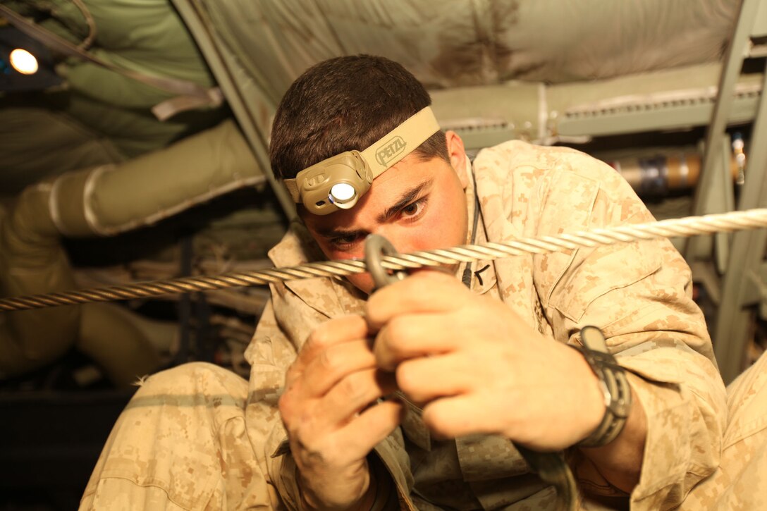 Pfc. Alejanero Uribarri, an air delivery specialist with 1st Marine Logistics Group (Forward), connects a parachute to the static line, which will automatically deploy the parachute when it is released off of a KC-130J.  Marines of Marine Aerial Refueler Transport Squadron 352, Detachment A, 3rd Marine Aircraft Wing (Forward), completed a section aerial delivery drop to Marines of 2nd Battalion, 1st Marine Regiment, in Helmand province, Afghanistan.  A section aerial delivery is comprised of two aircraft making a supply drop.  Bundles used during the drop are created using thick cardboard pallets and boxes of water, food or ammunition.  Parachutes are then attached to the top of the bundles and rigged for automatic deployment as they leave the aircraft during flight. It took the Marines about two hours, from preparing the aircraft to releasing the bundles, to successfully complete the mission. Through teamwork, the VMGR-352, Det. A, Marines continually support coalition forces on the front lines and in isolated locations by delivering the supplies they need in the quickest manner possible.
