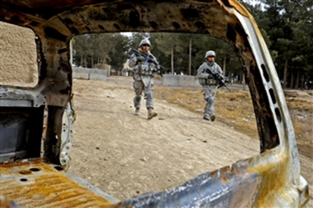 U.S. Army Pfc. Carlos Ortiz, left, and Spc. Kevin Vo walk past a burned-out car during a trip to a village near Shahr-e Safa, Afghanistan, Jan. 19, 2011. Members of Provincial Reconstruction Team Zubul visited the village to assess future projects and speak to elders about issues within the village.