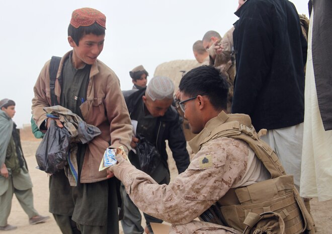 Sergeant Channy Yin, a food service specialist with Delta Company, 3rd Light Armored Reconnaissance Battalion, 1st Marine Division (Forward), hands cookies to an Afghan boy a visit to a local school, Jan. 19, 2011. Channy, a 25-year-old native of Lawrence, Mass., and his fellow Marines and sailors gave the children hygiene products and snacks and even played a small soccer game.