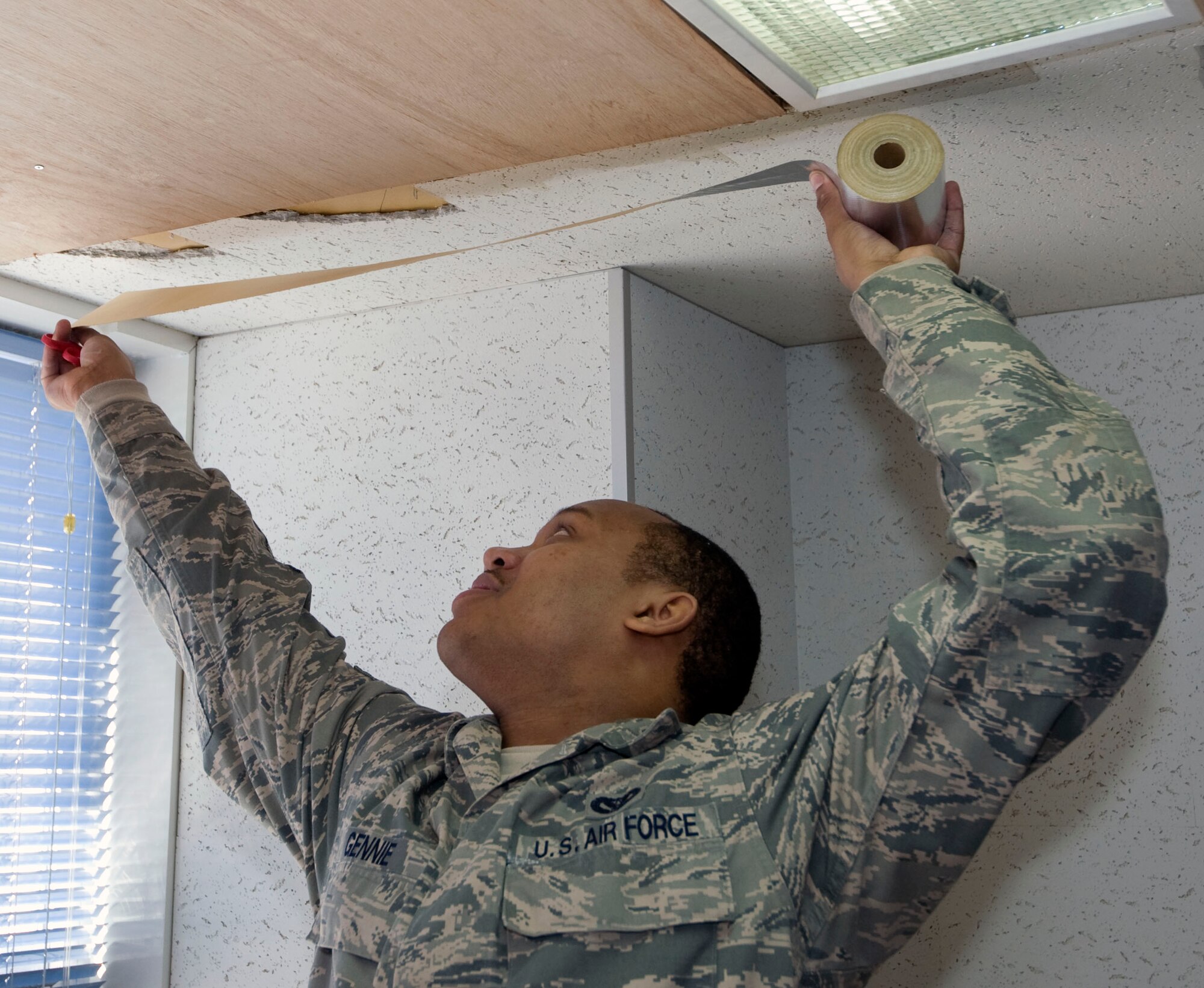 U.S. Air Force Senior Airman Ricky Gennie , 35th Civil Engineer Squadron, structural journeyman, applies silver tape on the edges of plywood on the ceiling of Cummings Elementary School, Misawa Air Base, Japan, Jan. 18, 2011. The water damage affected many rooms and hallways, including the library. (U.S. Air Force photo by Tech. Sgt. Russell McBride/Released)