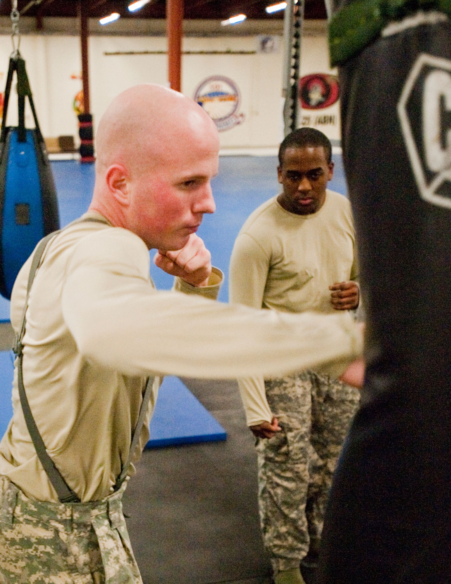 Spc. Layton Warstler, 545th Military Police Company knees a punching bag at the new Arctic Warrior Combatives Academy, Tuesday as Spc. Wayne Gittens, 545th MP Co. looks on. The academy opened Jan. 12 to Soldiers and Airmen.  (U.S. Air Force photo/Airman 1st Class Christopher Gross)