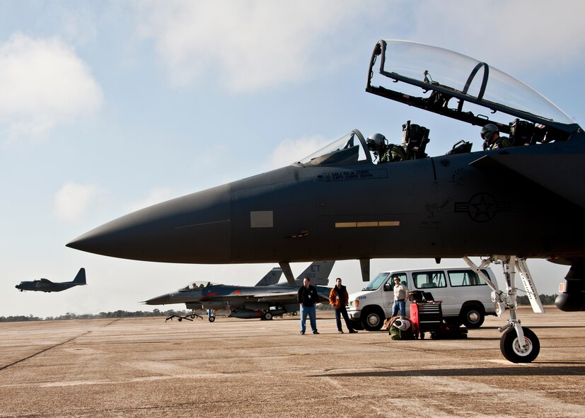 An F-15E and two F-16s from the 46th Test Wing prepare to taxi out as a 919th Special Operations Wing C-130E lifts off from Eglin Air Force Base, Fla., Jan. 18.  The Strike Eagle flew the first ever sortie with the new APG-82 radar.  The new radar replaces the 24-year-old APG-70 radar system.  (U.S. Air Force photo/Samuel King Jr.)