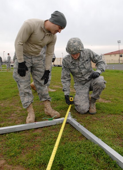 Senior Airman Seth Nobrega and Airman 1st Class Collin Pinkerton-Morrow, both aerial porters assigned to the 570th Global Mobility Squadron, ensure base measurements are even before constructing of an Alaskan Shelter during training for an upcoming inspection, Jan. 11. Members of the 615th Contingency Response Wing conduct periodic training to stay sharp for an upcoming Operational Readiness Inspection and its demanding mission. (U.S. Air Force Photo/Master Sgt Stan Parker)