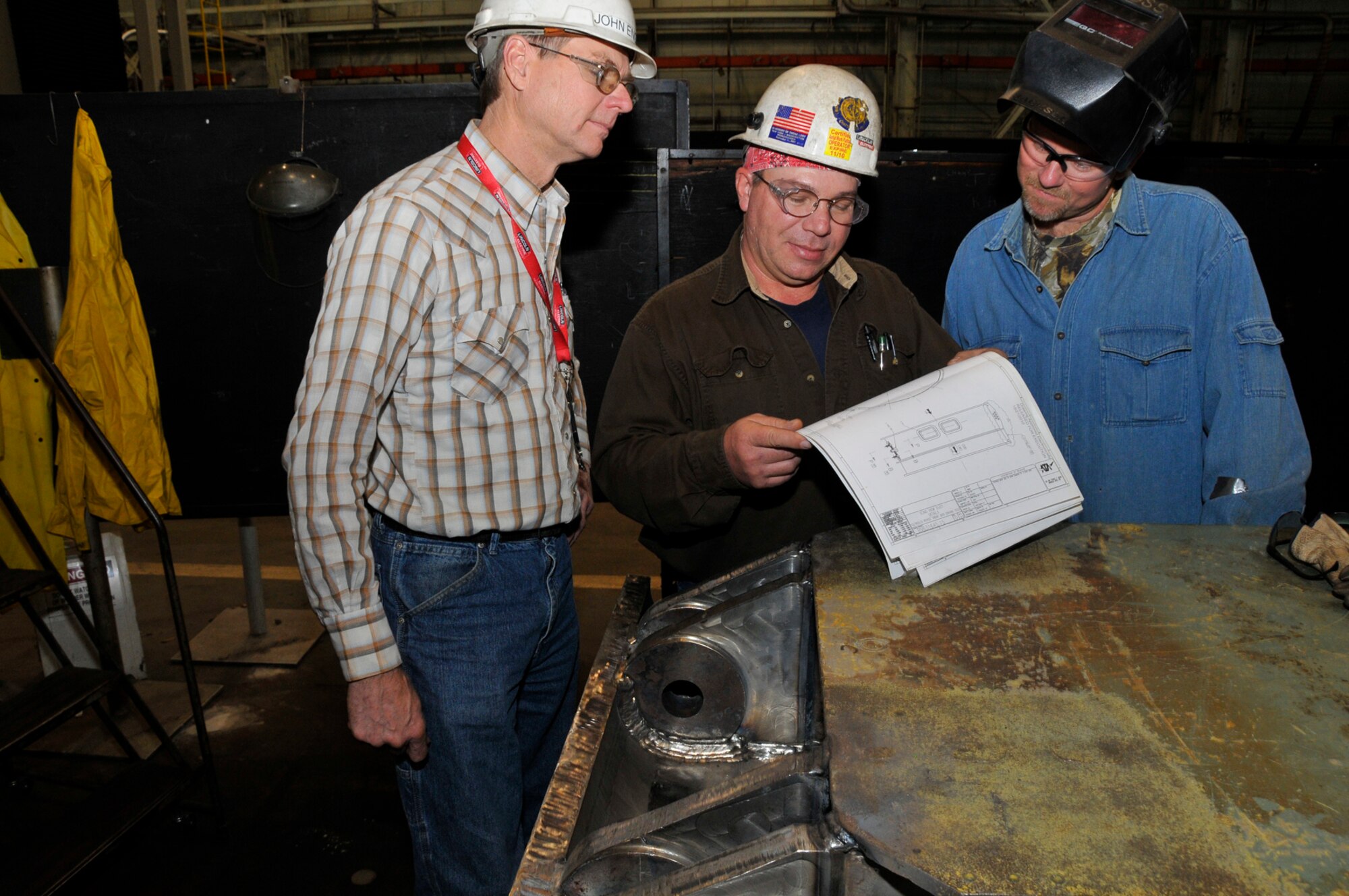 John England, left, inspects drawings specifying a total rebuild of a diffuser plate damaged in an equipment failure at AEDC’s Von Kármán Gas Dynamic Facility Wind Tunnel A.  Boilermakers Michael Dickey and Jeff Moss repaired the plate by bending plates of steel almost two inches thick and welding massive plates of dissimilar metals. (Photo by Rick Goodfriend)