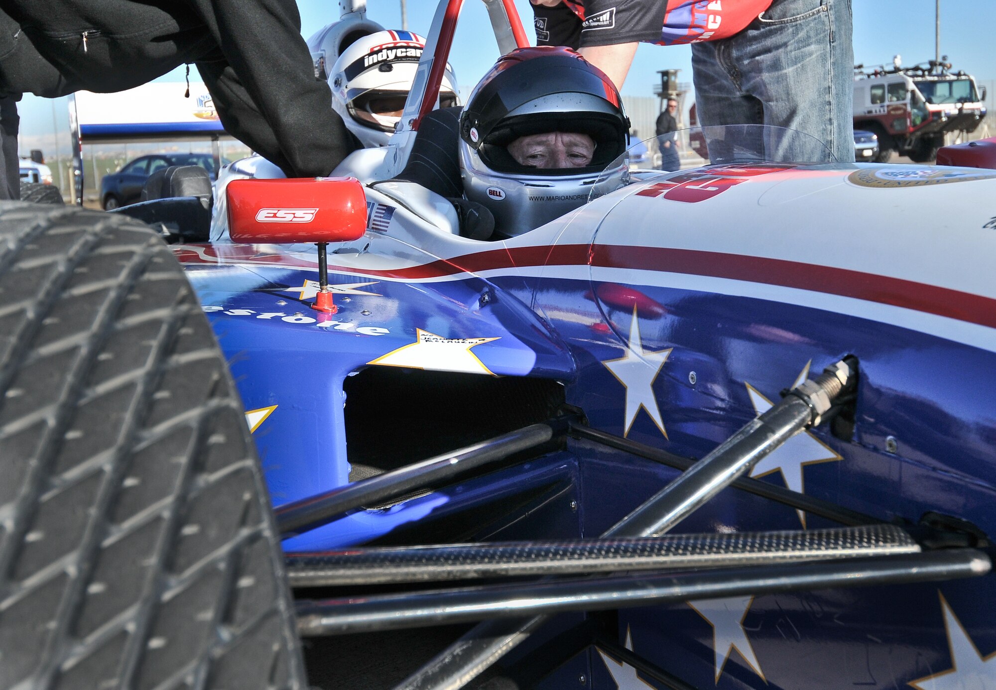 Mario Andretti, legendary four time Indianapolis 500 race winner, waits as his crew secures demo ride winner Staff Sgt. Jayson Escalera from the 39th Logistics Readiness Squadron, Jan. 19, at Incirlik Air Base, Turkey. More than 30 individuals were chosen to ride in the Indy 500 racecar.. The Indy 500 Centennial Tour, coordinated by Morale Entertainment Foundation and Armed Forces Entertainment, in conjunction with the IZOD Indy Car Series and the Indianapolis Motor Speedway, is a 10-day morale trip to Europe and the Middle East with the goal of boosting the morale of more than 10,000  servicemembers. The team, which includes Indianapolis 500 winners Mario Andretti, Johnny Rutherford and Al Unser Jr. plus Indy 500 veterans Sarah Fisher, Davey Hamilton, Larry Foyt and Firestone Indy Lights race winner Martin Plowman, spoke with the winners and signed autographs during the visit. (U.S. Air Force photo by Staff Sergeant Alexandre Montes/Released)