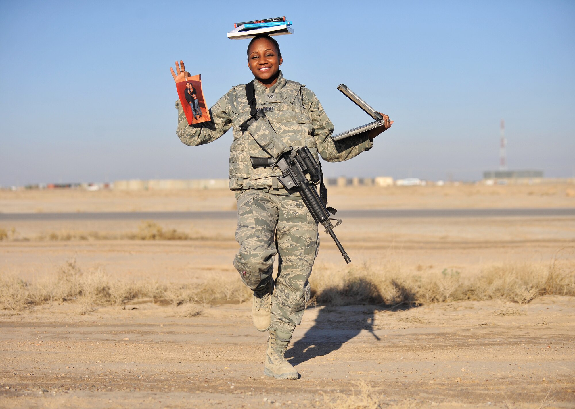Staff Sgt. Gissell Gilbert, the noncommissioned officer in charge of the automated data processing and equipment of Contingency Operating Base Speicher, poses for a photo while holding a laptop and a picture of her and her husband balancing schoolbooks on her head Jan. 21, 2011 on COB Speicher, Iraq. (U.S. Air Force photo by Senior Airman Andrew Lee/Released)