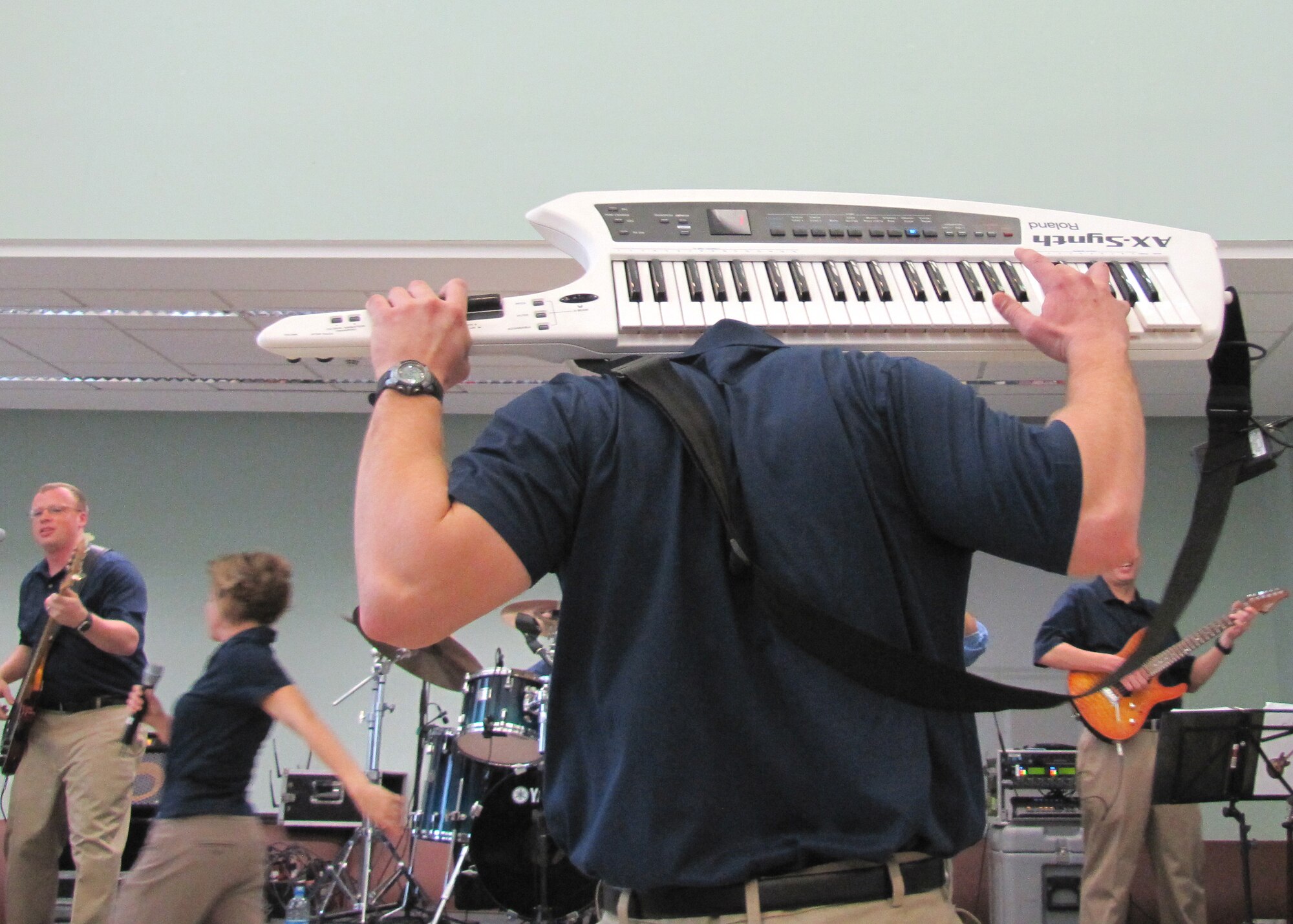 Pianist, Senior Airman Adam Braatz, flawlessly plays a keytar behind his head. A keytar is a lightweight keyboard built similar to a guitar. Approximately 600 students in an American secondary school at an undisclosed location in Southwest Asia gathered in their cafeteria for a live performance by the U.S. Air Forces Central rock band, Starlifter, Jan. 19.
