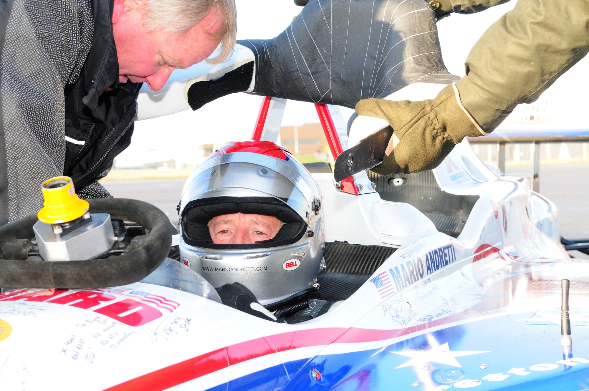 RAF MILDENHALL, England – Racing legend Mario Andretti, winner of 12 Formula 1 Grand Prixs, second place in all-time wins and all-time pole position winner in IndyCar racing, sits patiently in the two-seater IndyCar as final adjustments and checks are made to the car before he drives it down the flightline here Jan. 21, 2011. Base members from both RAFs Mildenhall and Lakenheath took turns in the passenger seat of the race car, and reached speeds of up to 150 mph as Andretti, along with British driver Martin Plowman, an Indy Lights racing driver, gave them the thrill of a lifetime. (U.S. Air Force photo/Karen Abeyasekere)