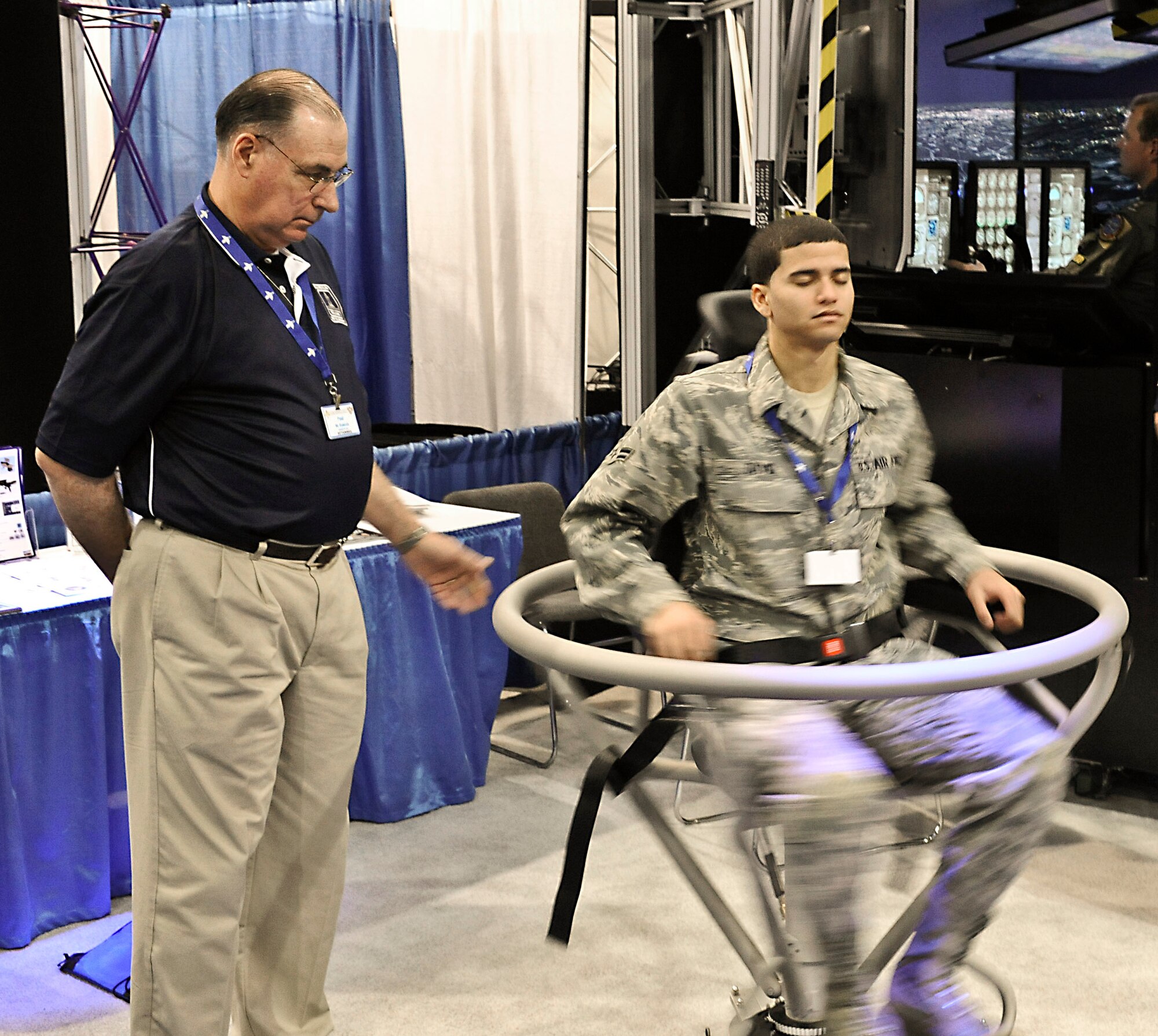 Paul Ramsey, Randolph Trainer Development, watches as Airman 1st Class Brett David, 81st Training Group at Kessler Air Force Base, Miss., tries out the barany chair Jan. 21 during the 2011 Air Education and Training Command Symposium and Expostion in San Antonio, Texas. (U.S. Air Force photo/ by Don Lindsey) 