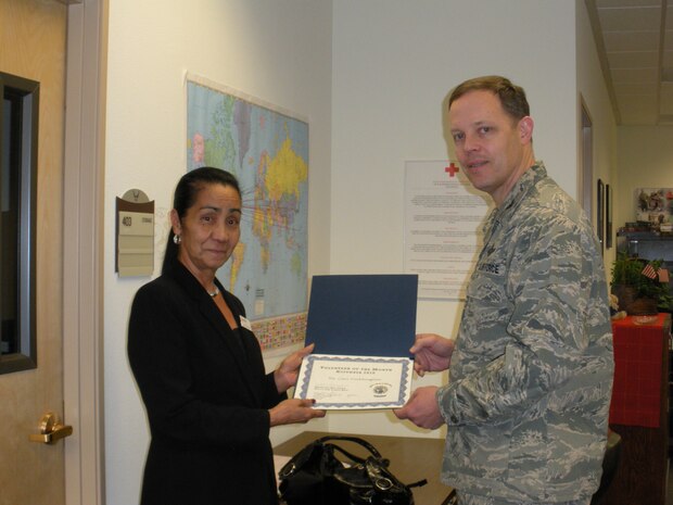Col. Steven Garland, 99th Air Base Wing commander, presents a coin and a certificate of appreciation to Cari Pocklington, the December volunteer of the month, Jan. 18 at the American Red Cross Branch Office.  (Courtesy photo)