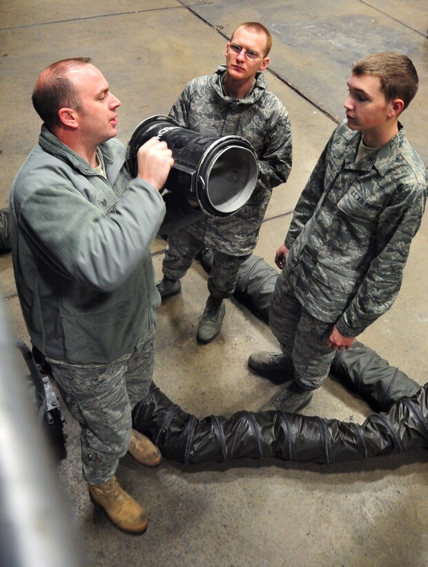 (Right to left) Airman Mark Vadnais and Airman 1st Class Christian mains, 28th Aircraft Maintenance Squadron able chiefs, are taught how to attach a connector to an airflow hose by Staff Sgt. Chris Dieball, 28th AXMS crew chief instructor, at Ellsworth Air Force Base, S.D., Jan. 21.  The connector is used to fasten the airflow hose to a B-1B Lancer in order to cool off electrical systems during maintenance. (U.S. Air Force photo/Senior Airman Anthony Sanchelli)