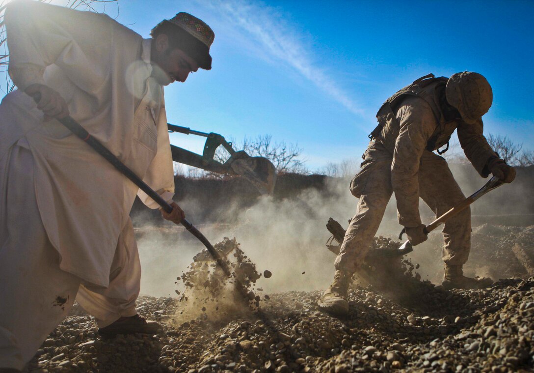 Cpl. Steven Artis, a combat engineer with Combat Logistics Battalion 3, 1st Marine Logistics Group (Forward), spreads gravel while an Afghan citizen offers assistance near Katoray, Afghanistan, Jan. 30. Marines with CLB-3's Engineer Company have completed more than 10 miles of road repair on the most heavily trafficked route in Afghanistan's Helmand province.
