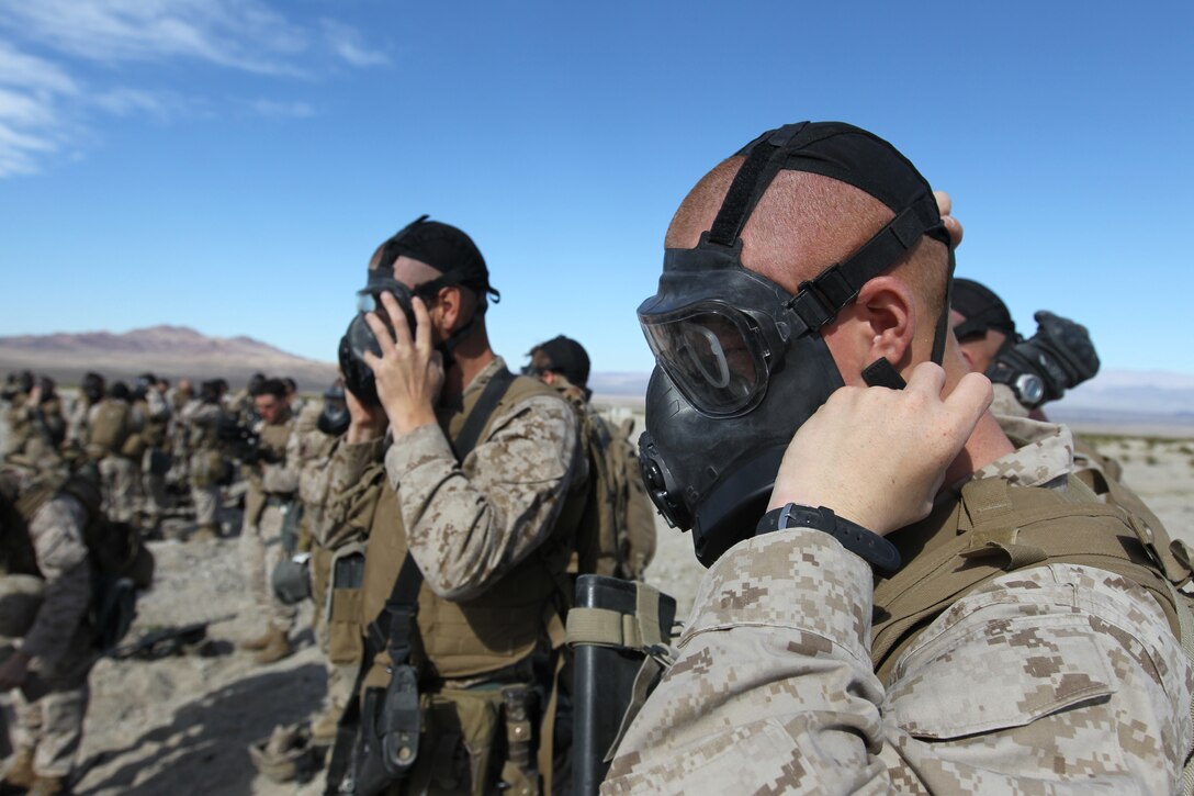 Marines and sailors with Company E., 2nd Battalion, 7th Marine Regiment, adjust their masks before performing an outdoor gas exercise at range 210 Jan. 26, 2011. The Marines and sailors in full protective gear take turns marching through the cloud of gas to test and become acquainted with their new gear.