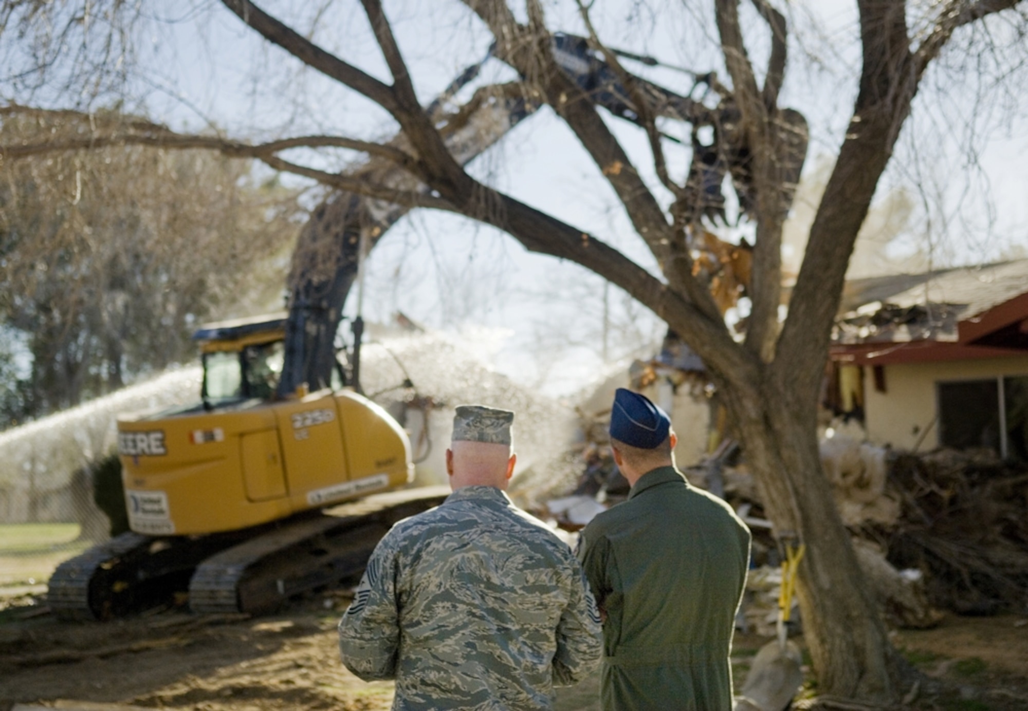 Chief Master Sgt. Bill Thomaston (left), 95th Air Base Wing command chief and Maj. James Spencer, Air Force Flight Test Center commander’s executive officer, look on as Brig. Gen.Robert C. Nolan II, Air Force Flight Test Center commander, commences a demolition project by tearing down the project’s first house. (Air Force Photo by Rob Densmore)