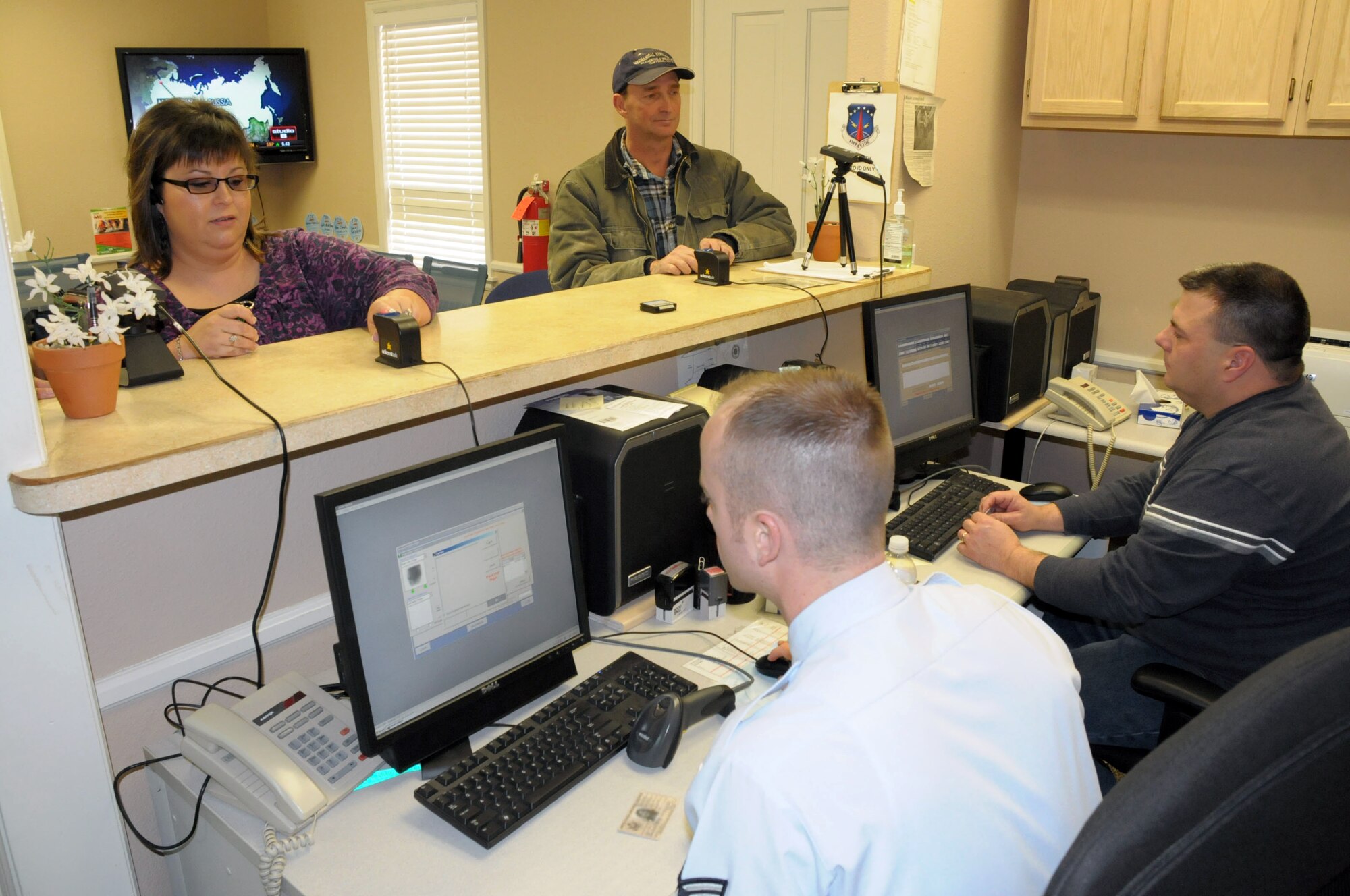 Mrs. Lori Chavez, base chapel assistant, has her finger scanned as Mr. Richard Phaff, contractor for Mechanical Systems, is assisted by Staff Sgt. Derek Wader and  Kendall Remines, both from 90th Security Forces Squadron, to have their military Common Access Cards renewed for the Defense Biometric Identification System. (U.S. Air Force photo by Blaze Lipowski)