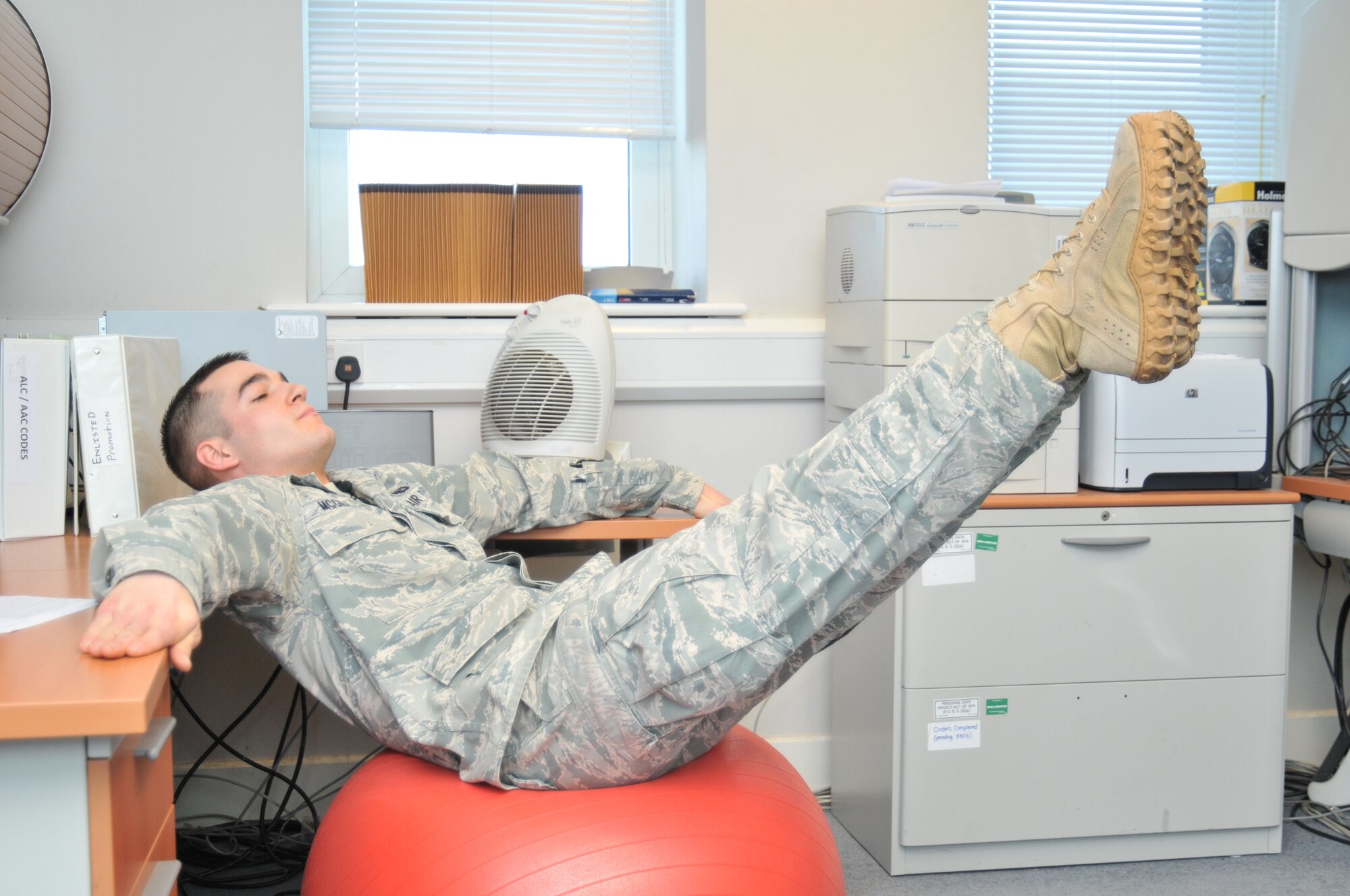 ROYAL AIR FORCE LAKENHEATH, England - Senior Airman Jared McGrady, 48th Force Support Squadron fitness and sports specialist, demonstrates a leg lift at his office, Jan. 18. Exercises such as this, using a stability ball that can be easily stored under a desk, are quick and easy ways to squeeze fitness into a busy work day. (U.S. Air Force photo/Senior Airman David Dobrydney)