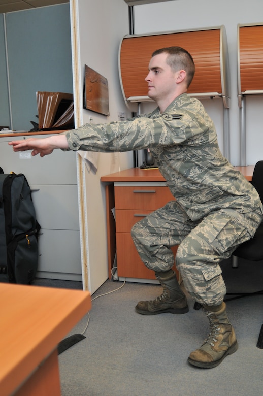 ROYAL AIR FORCE LAKENHEATH, England - Senior Airman Travis Ringer, 48th Force Support Squadron fitness and sports specialist, demonstrates how to do a squat in an office, Jan. 19. Exercises such as this are an easy way to get in at least 30 minutes of physical activity each day. (U.S. Air Force photo/Senior Airman David Dobrydney)