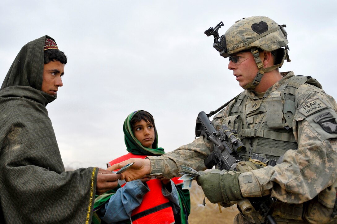 U.S. Army Sgt. Robert Smith pays an Afghan boy for assisting in the collection of unexploded ordnance outside Stronghold Dog, Afghanistan, Jan. 29, 2011. The program, Cash for Work, is a partnership with local communities, providing income for day laborers and the collection of unexploded ordnance. Smith is assigned to the 101st Airborne Division's 2nd Battalion, 502nd Infantry Regiment.
