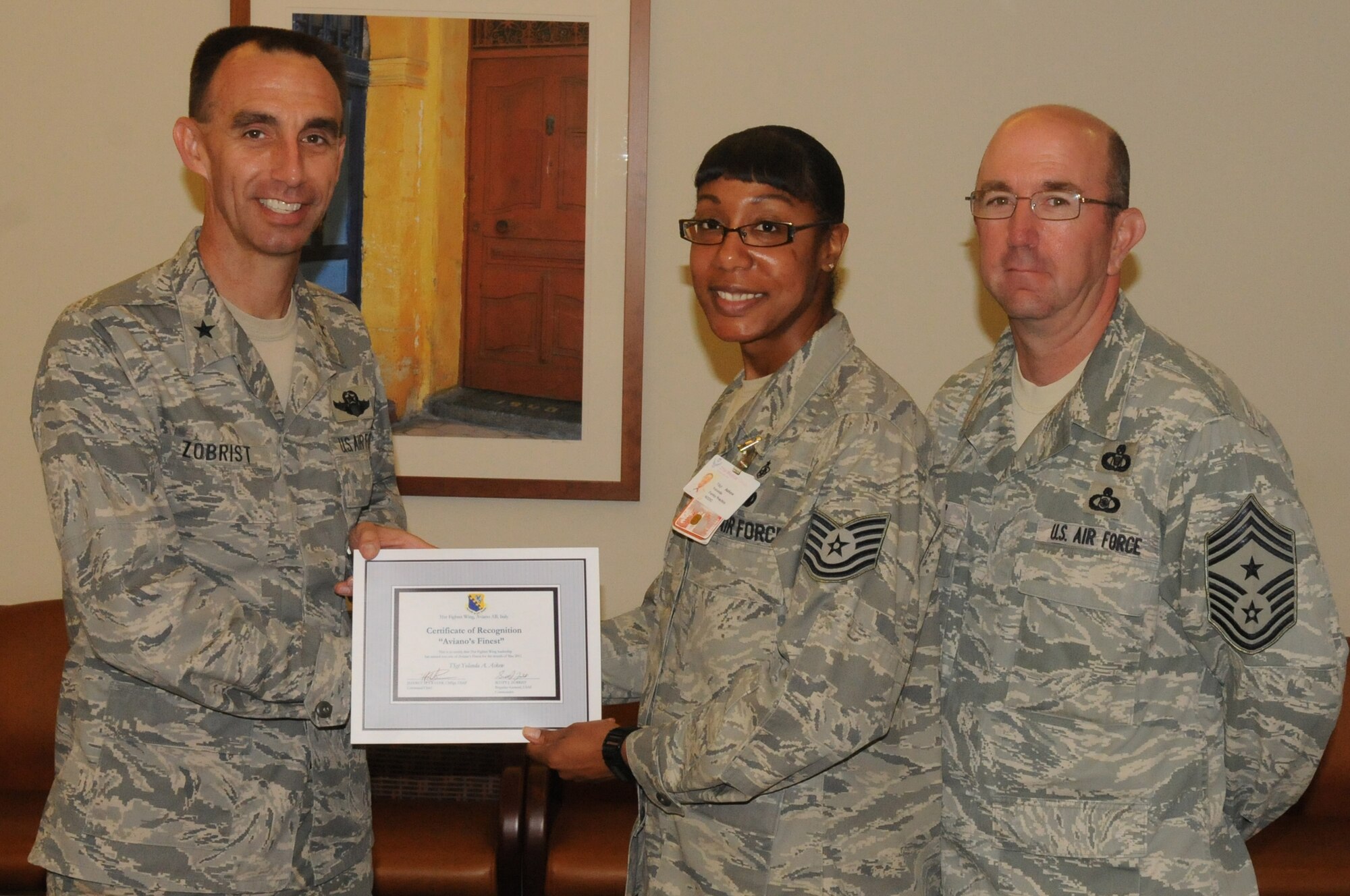 Brig. Gen. Scott J. Zobrist, 31st Fighter Wing commander, along with 31 FW Command Chief Master Sgt. Jeffrey Craver, congratulate Tech. Sgt. Yolanda Askew, 31st Medical Operations Squadron family practice technician, on her selection as one of Aviano’s finest.