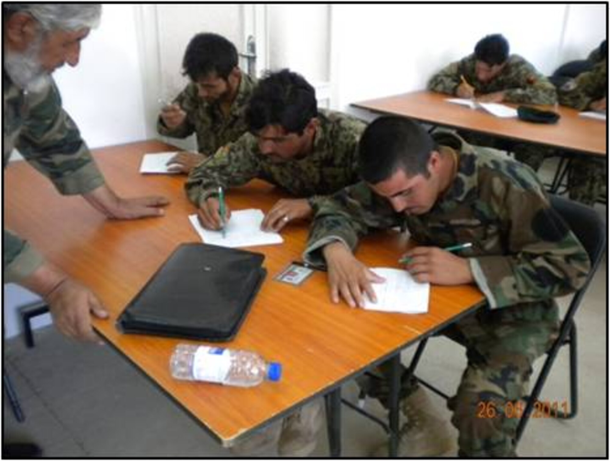 SHINDAND, Afghanistan – An Afghan teacher administers the literacy portion of the promotion exam to two Afghan Air Force members June 27.  In addition to the literacy test, AAF members also finished the physical fitness portion as well.  According to personnel officials, promotion testing for the ranks of E-4 to E-5 and E-5 to E-6 are the only ranks handled directly by the AAF per Ministry of Defence policy with all other ranks handled centrally through the MoD on an annual basis.  (U.S. Air Force courtesy photo)   
