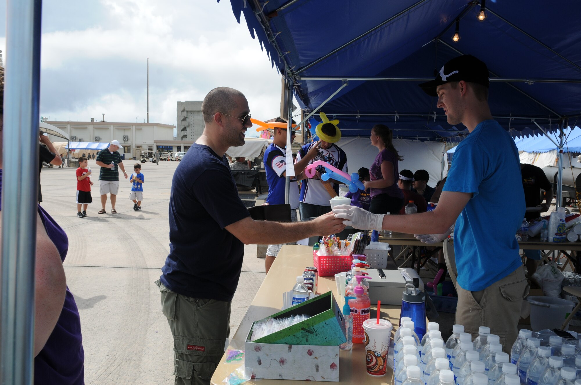 Master Sgt. Anthony Bertschy, 18th Communications Squadron first sergeant, purchases a snow cone from Airman 1st Class Benjamin Quade, 18th CS cyber transport technician, at the squadron's booth July 1 during AmericaFest at Kadena Air Base, Japan. AmericaFest took place on the Kadena flight line July 1 and 2. (U.S. Air Force photo/Staff Sgt. Amanda Savannah)