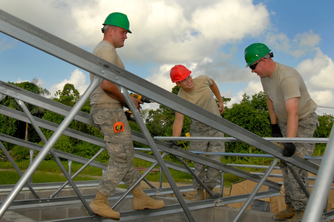U.S. Air Force Senior Airman Trevor Krcil, left, Senior Airman Karl McClamma, center, and Master Sgt. Edward Ness, right, adjust perlins before fastening them to ceiling trusses at the Lower Technical School IV in Paramaribo, Suriname, July 2, 2011. Krcil and Ness are assigned to the 114th Fighter Wing Civil Engineer Squadron, and McClamma is assigned to the 556th Red Horse Squadron.