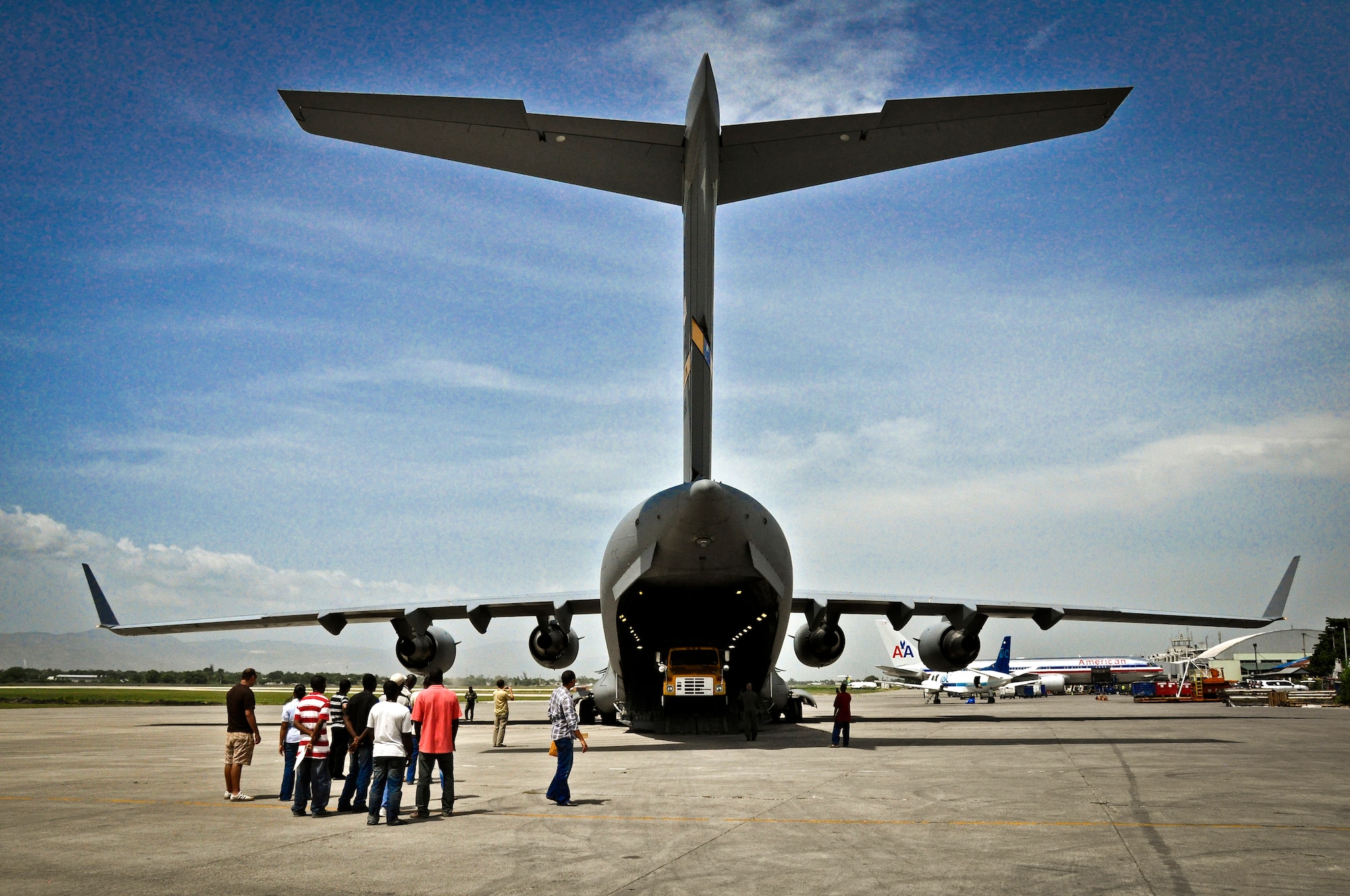 Humanitarian aid workers wait patiently for a dump truck to roll of the ramp of a C-17 Clobemaster III during an aid mission to Haiti on July 1, 2011. The truck was delivered with over 50,000 pounds of rice to the island in support of the Denton program. (U.S. Air Force Photo/SSgt. Rashard Coaxum) 