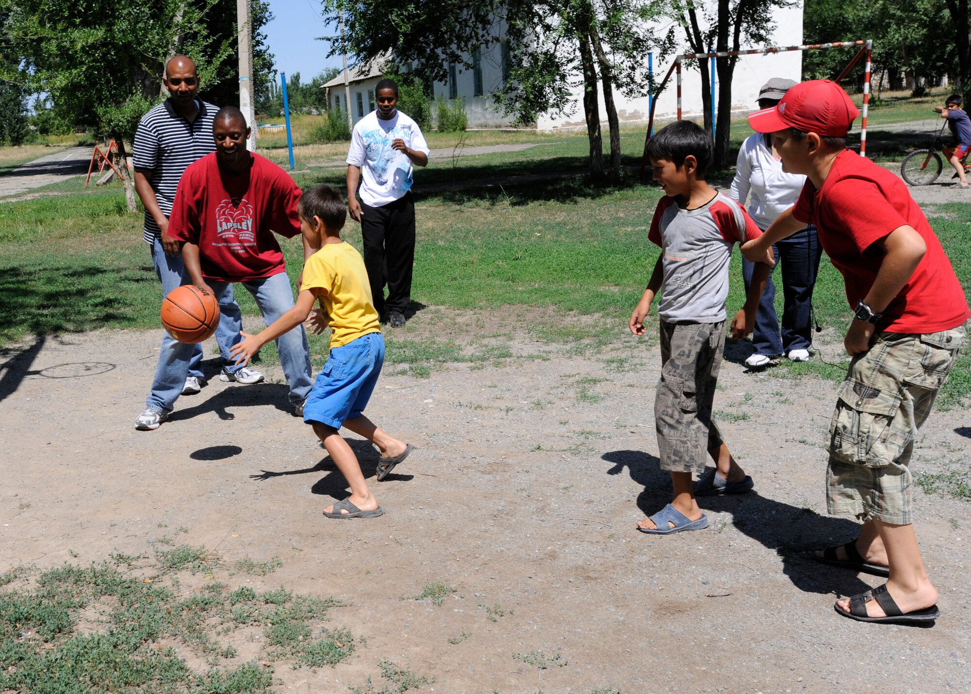 KAMYSHANOVKA, Kyrgyzstan – Airmen from the 376th Expeditionary Communications Squadron watch as a Kyrgyz child dribbles toward a basketball hoop during the group’s visit to the Kamyshanovka School July 1. The Transit Center at Manas Airmen donated a public address system and sporting equipment to the village. They then spent the afternoon playing games with students and interacting with village officials. (U.S. Air Force photo/Tech. Sgt. Tammie Moore)