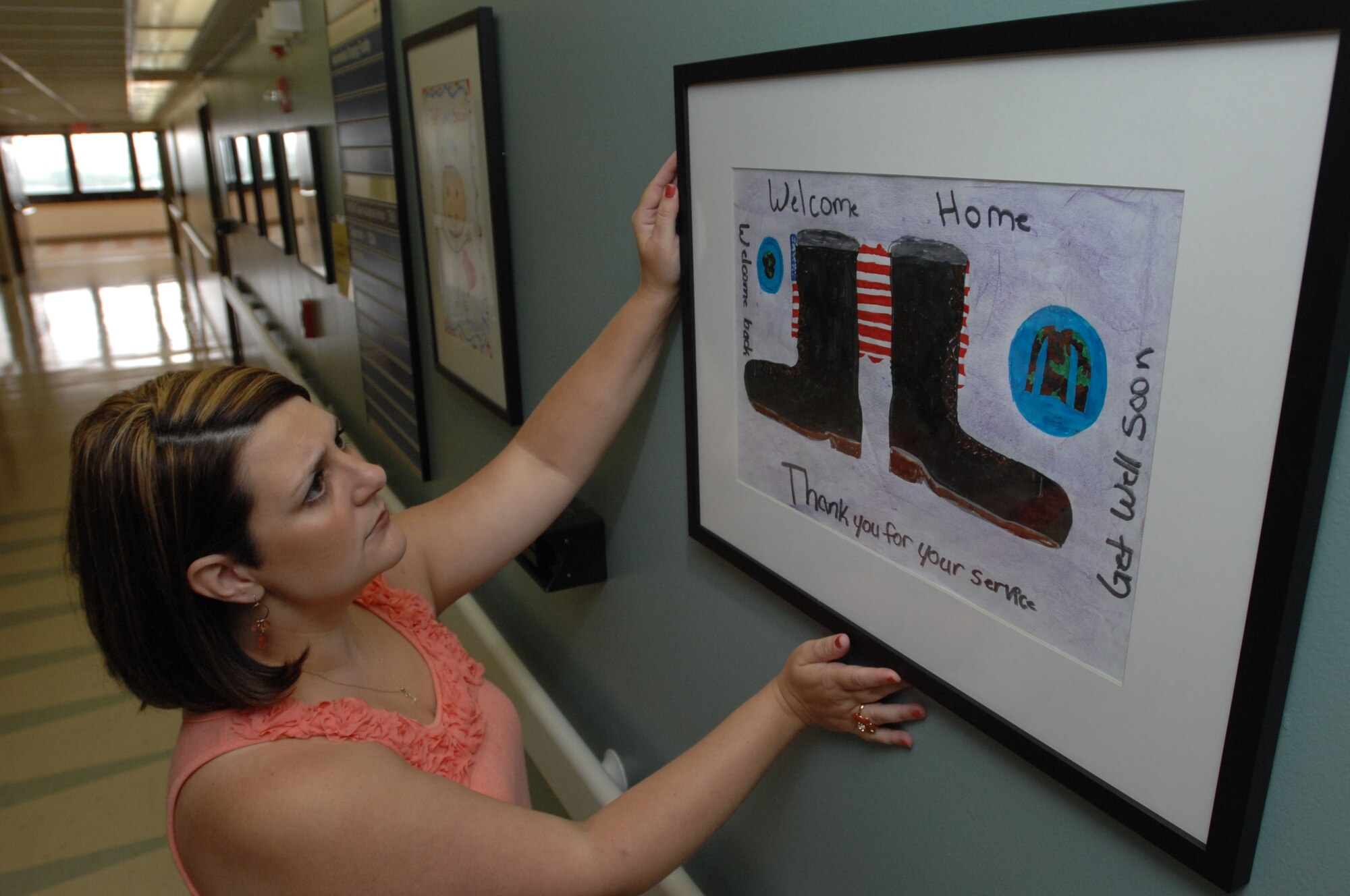 Tory Johnson, Wilford Hall?s hospital interior designer, adjusts framed artwork mounted in the hallway of the new Contingency Aeromedical Staging Facility here on June 13, 2011.  Nearly 390 elementary school children from several San Antonio schools donated their artwork to the CASF to lift the spirits of the ill and injured servicemembers returning from overseas. (U.S. Air Force photo/Staff Sgt. Robert Barnett)