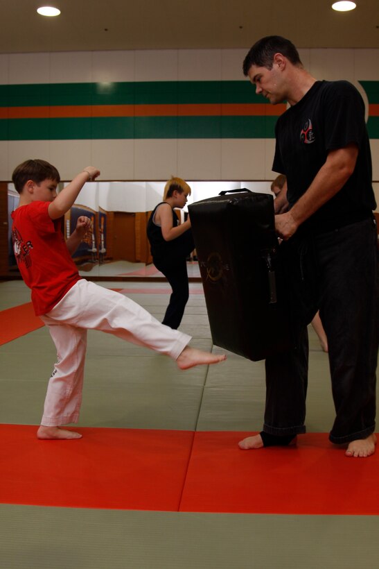Brian C. Mallon, an IronWorks Gym karate instructor, holds a foam pad for Jesse Baker, an 8-year-old whitebelt karate student, to practice Baker’s kicks and punches during a children’s karate class at the martial arts dojo in IronWorks Gym here July 7. The karate class taught the students self-defense manuevers.