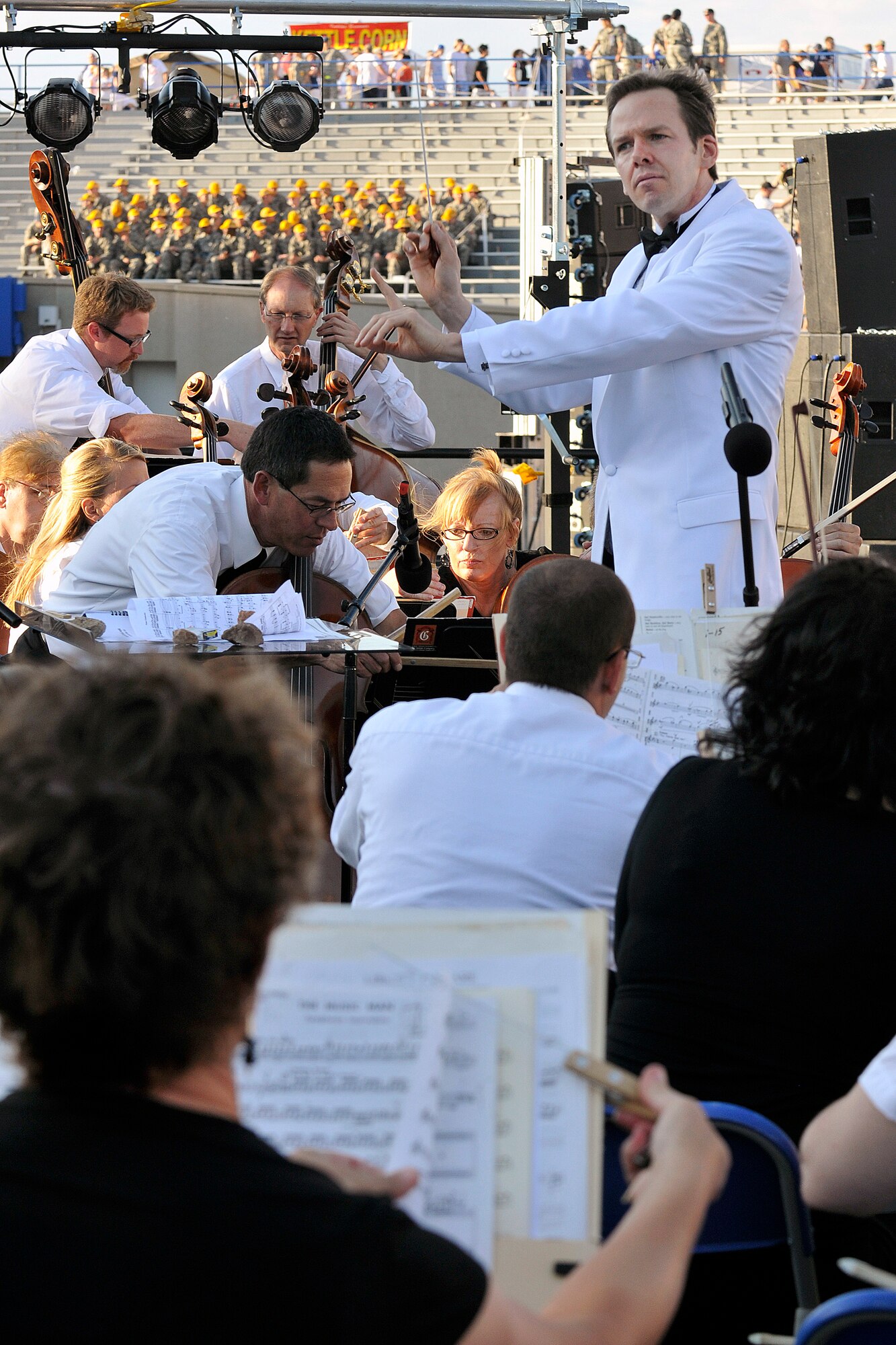 Thomas Wilson conducts a Colorado Springs Philharmonic performance in Falcon Stadium at the Air Force Academy July 4, 2011, while in the background, basic cadets get some welcome down time from Basic Cadet Training. Wilson, the philharmonic's associate conductor, began studying piano at age 4 and later learned the trumpet, percussion, string bass and voice. (U.S. Air Force photo/Megan Davis)
