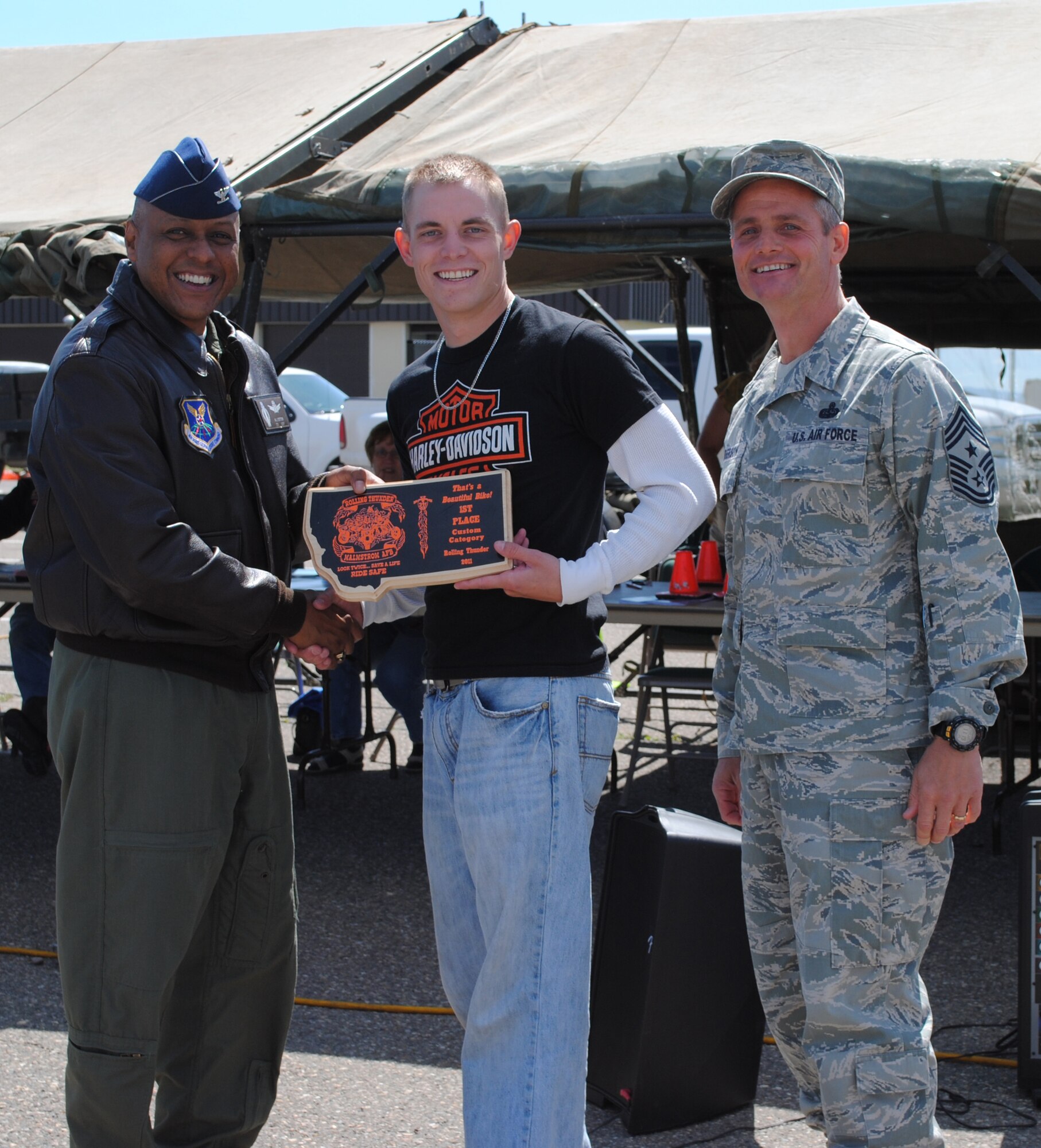 Brig. Gen. (Sel) Anthony Cotton, 341st Missile Wing commander, presents the winning placqu for the custom motorcycle class to Senior Airman Jarod Ruud, 819th RED HORSE Squadron pavement and construction apprentice, as Chief Master Sgt. Charles Anderson, 341st MW command chief, looks on.