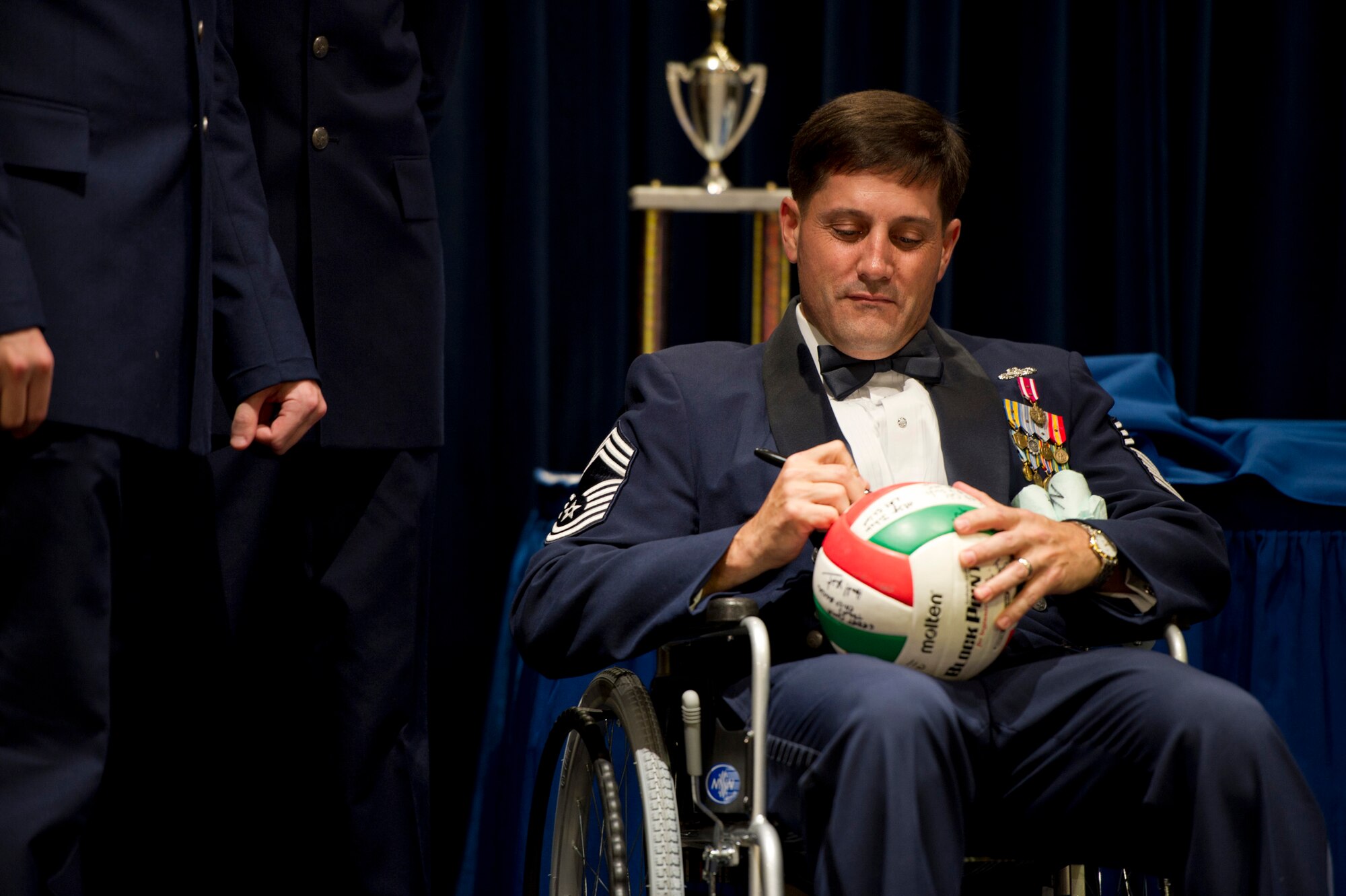 YOKOTA AIR BASE, Japan -- Chief Master Sgt. Chief Cornell, 374th Maintenance Group superintendent, signs the Airman Leadership School volleyball while sitting in a wheelchair during the ALS Class 11-E graduation ceremony at Yokota Air Base, Japan, July 7, 2011. The Airmen versus chiefs volleyball tournament is a time-honored tradition for Airmen Leadership Schools, as well as "roasting" each team during the graduation. The chiefs won the tournament, two games to one, and were given the honor of signing the volleyball. The wheelchair was presented by the Airmen to the chiefs to assist them in their "old age." (U.S. Air Force photo/Staff Sgt. Samuel Morse)