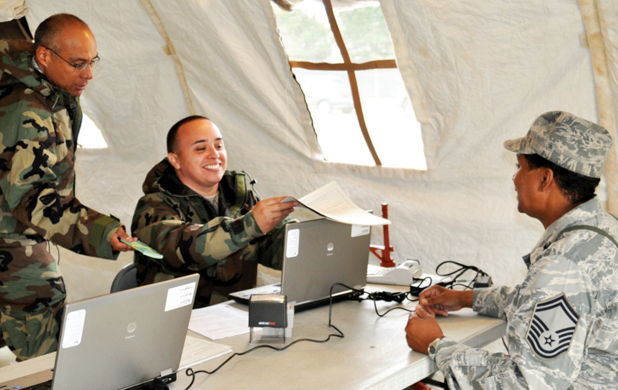 Tech. Sgt. Alvin Bartolome (standing) and Senior Airman Roy Jaramillo, both 452 AMW/FM customer service technicians and members of Team A for the Mini Top-Dollar exercise, work together to take care of a customer portrayed by Senior Master Sgt. Cynthia Cropper. Wearing part of the MOPP gear to identify her as an evaluator, Sergeant Cropper graded each team’s ability to organize and operate a deployed financial office.  (U.S. Air Force photo by Megan Crusher)
