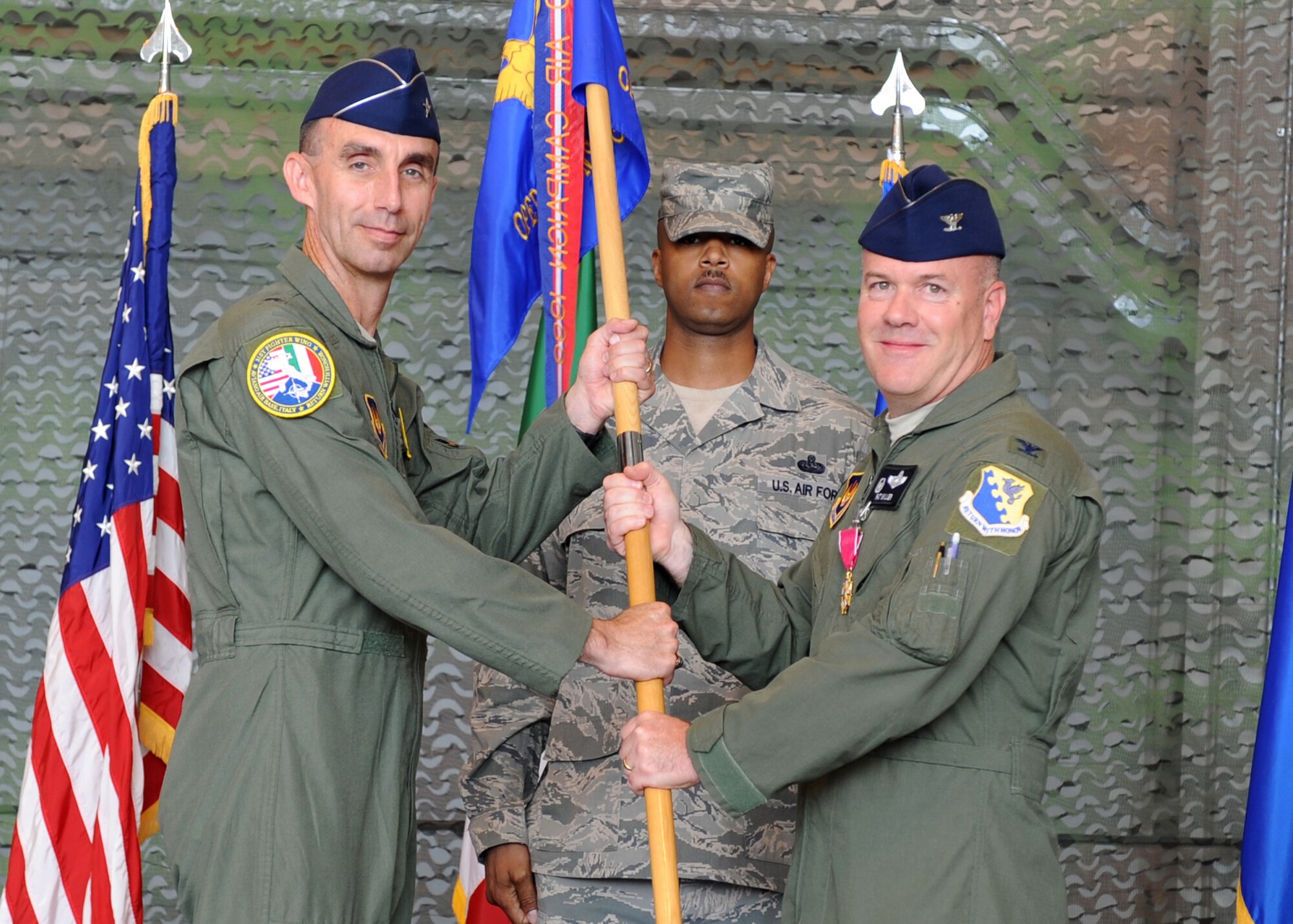 Col. Patrick J. S. Miller, former 31st Operations Group commander, passes the group guidon to Brig. Gen. Scott J. Zobrist, 31st Fighter Wing commander, during the 31st OG change of command ceremony July 7 at Aviano Air Base, Italy. Col. David W. Walker took command of the 31st OG. Prior to his current duties, Walker was a student at the Air War College at Maxwell Air Force Base, Ala. Miller will head to Yokota Air Base, Japan. (U.S. Air Force photo/Staff Sgt. Nadine Y. Barclay)