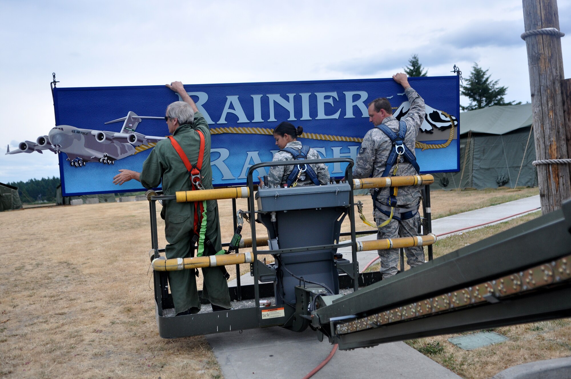 Mr. Craig Hays, left, Senior Airman Tiara Islam, center, and Tech. Sgt. Ivan Johnson, all 627th Civil Engineering Squadron structural support, prepare to hang the Rainier Ranch sign July 11 at Joint Base Lewis-McChord, Wash. Airmen have begun preparing 'Rainier Ranch' to host the multitude of United States and International teams when they arrive at the end of the month. (U.S. Air Force photo/Airman 1st Class Leah Young)