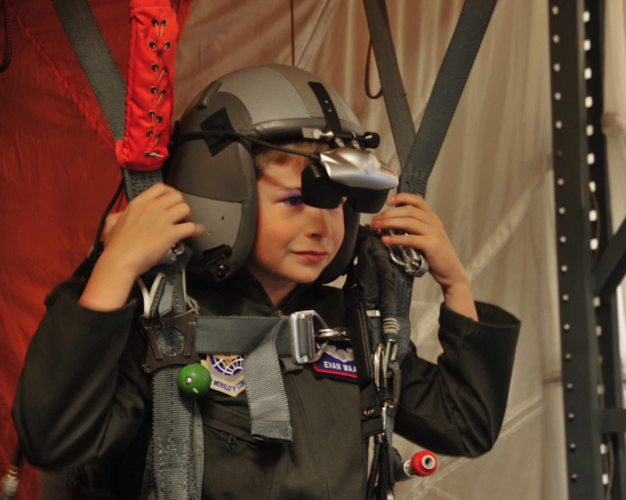 Evan Waara, "Pilot for a Day," prepares to "parachute" and land on a simulated naval ship July 7 at Joint Base Lewis-McChord, Wash. Evan had an opportunity to be strapped on a virtual reality parachute simulator as part of the Pilot for a Day Program. (Air Force photo/Staff Sgt. Frances Kriss)