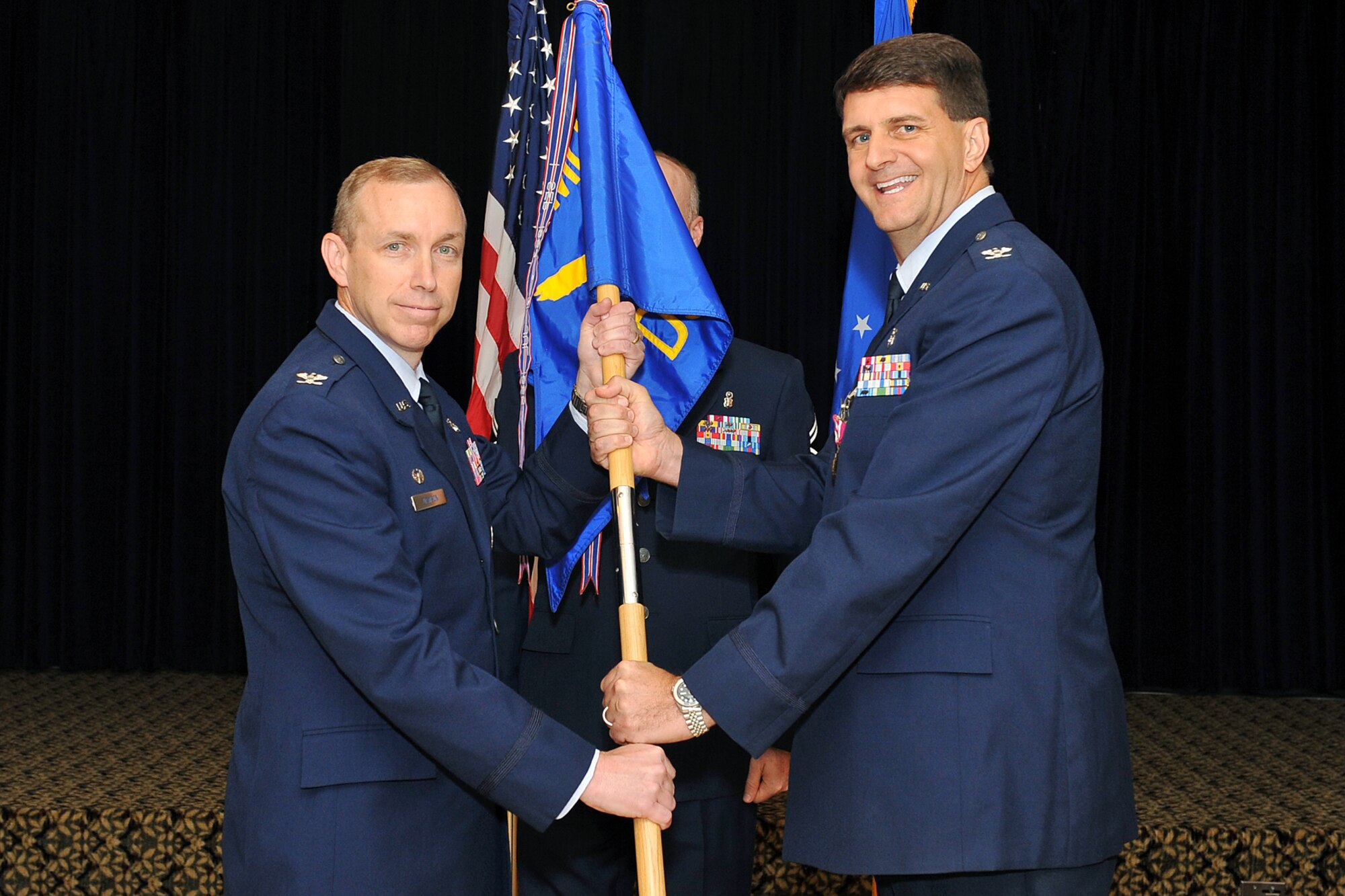U.S. Air Force Col. Robert Langsten, outgoing 55th Dental Squadron commander, relinquishes command and passes the squadron guidon to Col. Patrick Dawson, 55th Medical Group commander, during a change of command ceremony inside the Patriot Club on Offutt Air Force Base, Neb., July 15. (U.S. Air Force Photo by Charles Haymond/Released)