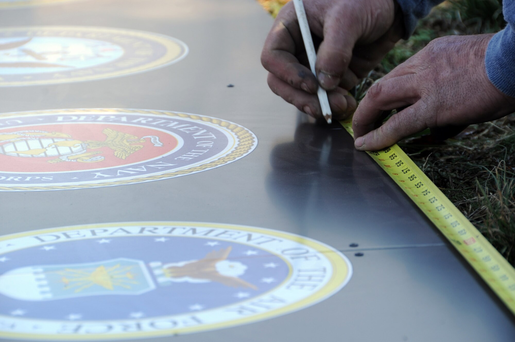 Workers measure to properly align Army, Navy and Air Force seals on the new sign for Joint Base McGuire-Dix-Lakehurst. McGuire Air Force Base, Fort Dix and Lakehurst Naval Air Engineering Station in New Jersey merged on Oct. 1, 2009, to become the Defense Department’s only tri-service base. (Courtesy Photo)   

